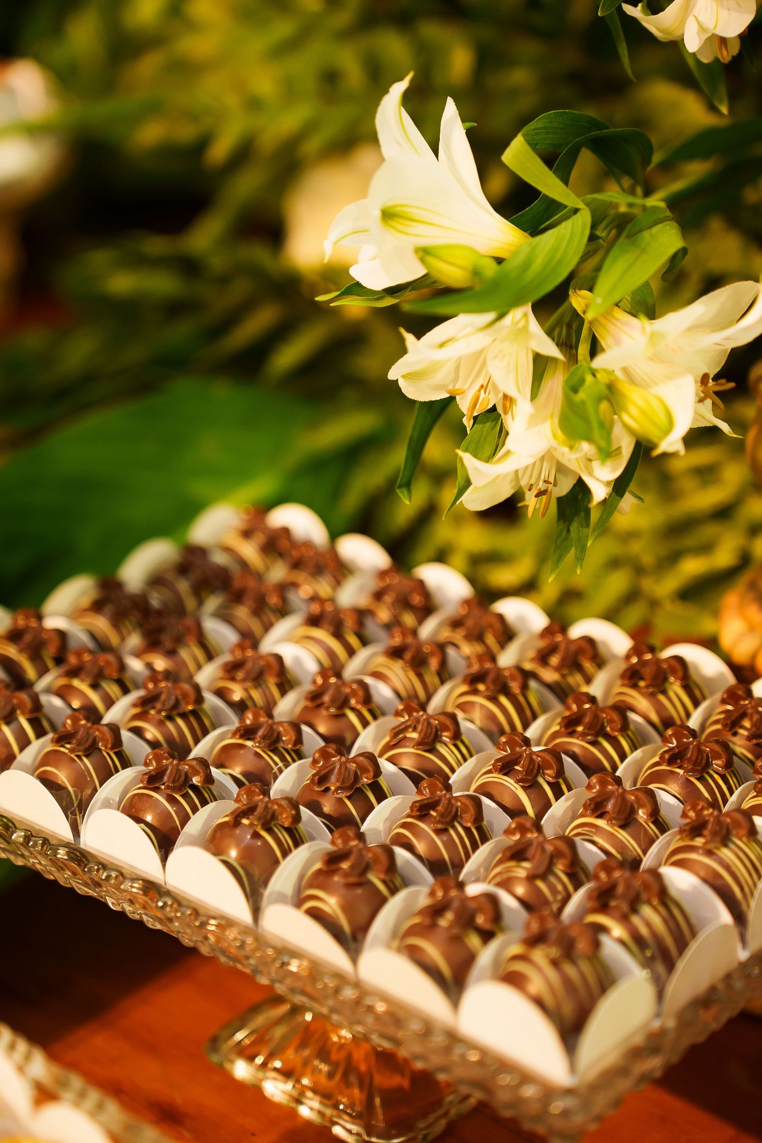 Elegant tray of chocolate-dipped wedding bonbons in white cups displayed with white lily flowers at a reception.