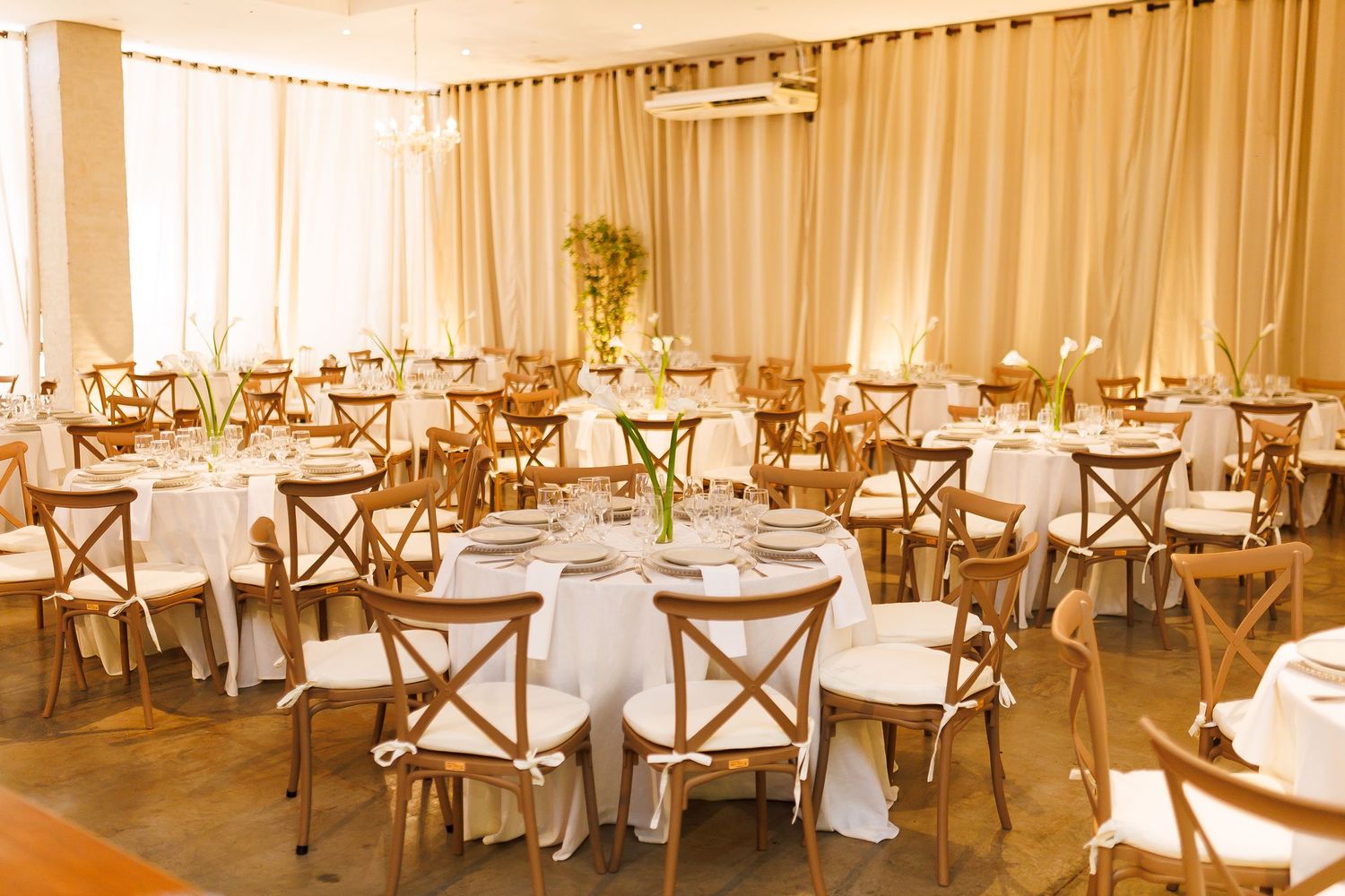 Elegant banquet hall with round tables, white linens, and wooden cross-back chairs set for a wedding reception.