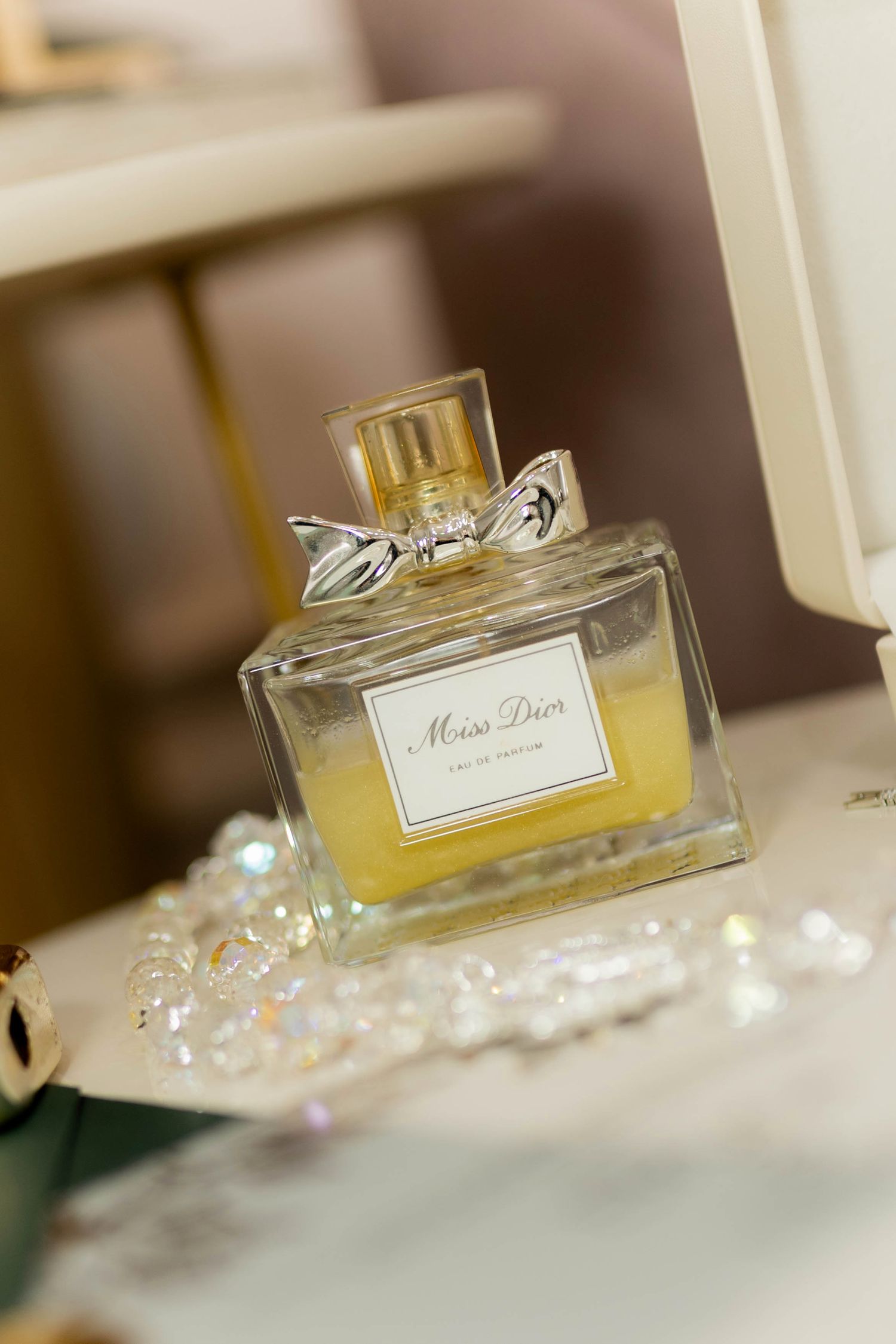 Miss Dior Eau de Parfum bottle with silver bow cap beside pearl jewelry on a vanity.