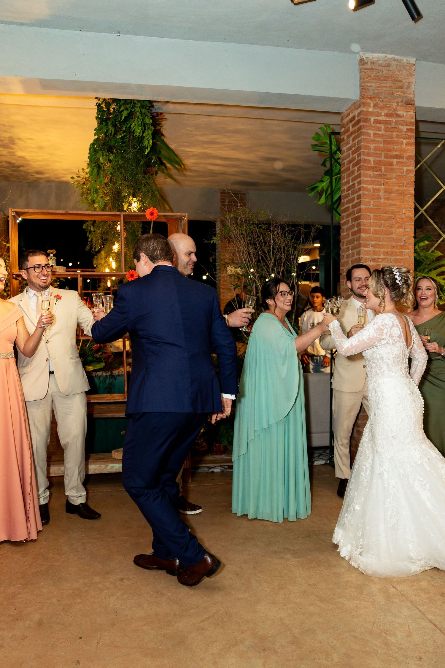 Wedding reception guests dancing joyfully, bride in white lace gown and guests in formal attire at elegant venue.
