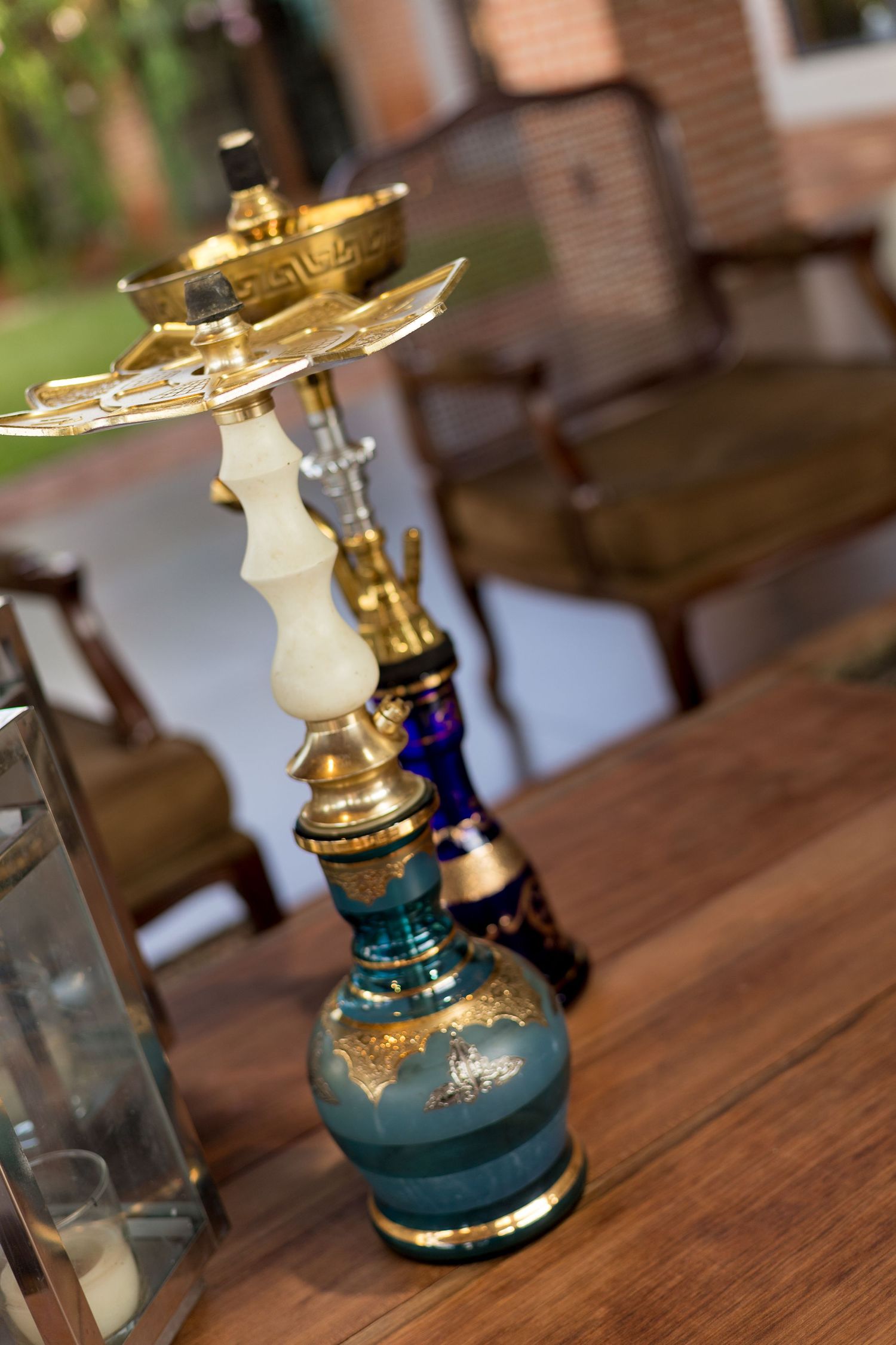 Ornate teal and gold hookah with decorative base displayed on a wooden table in an elegant outdoor setting.