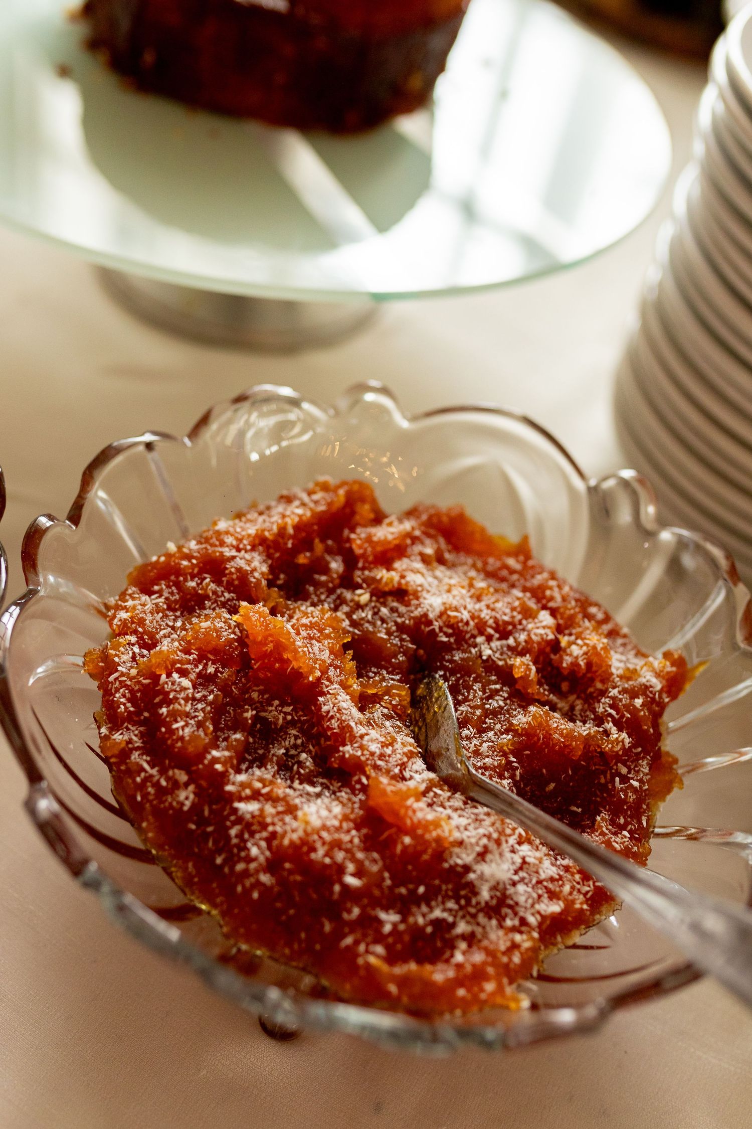 Close-up of a crystal bowl filled with sweet carrot halwa dessert, garnished with sugar, on a white tablecloth.