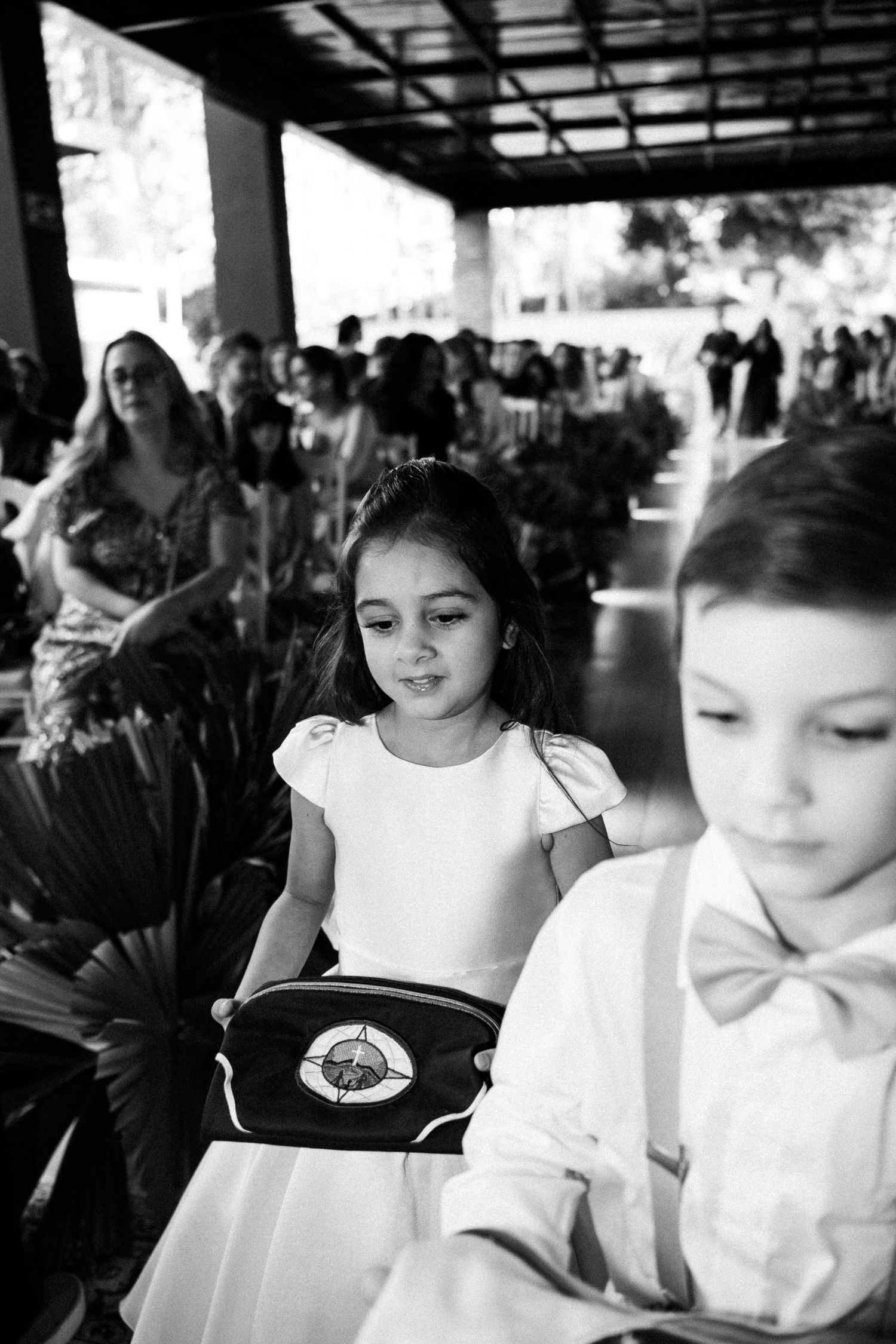 Black and white photo of children in formal attire at a wedding ceremony, girl in white dress holding a ring pillow.