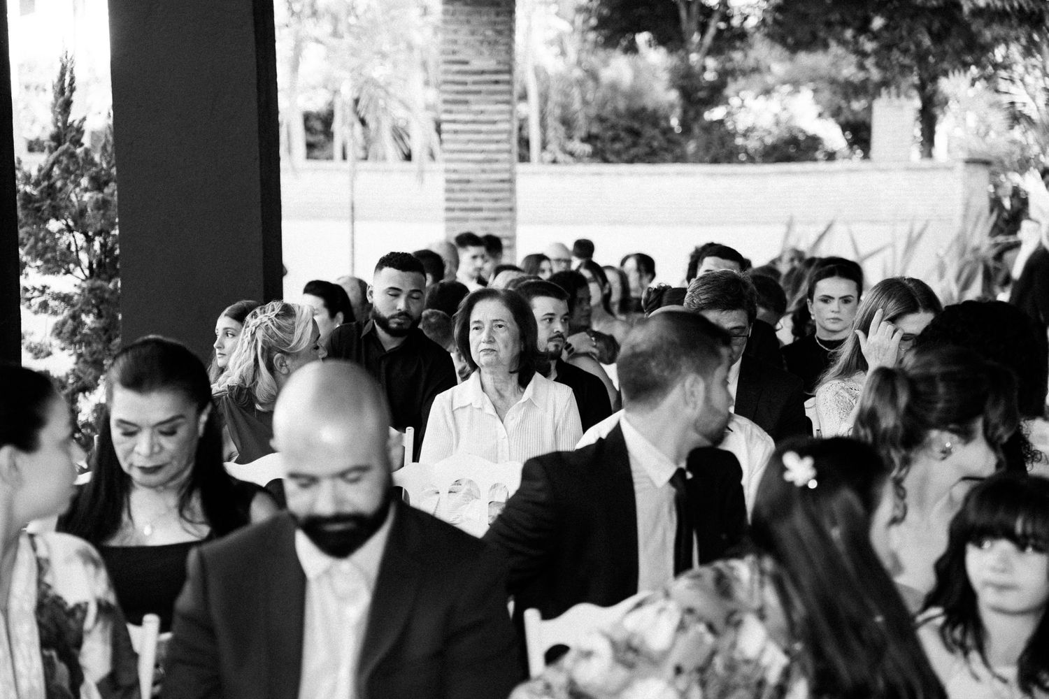 Black and white photo of elegantly dressed wedding guests gathered at an outdoor ceremony venue.