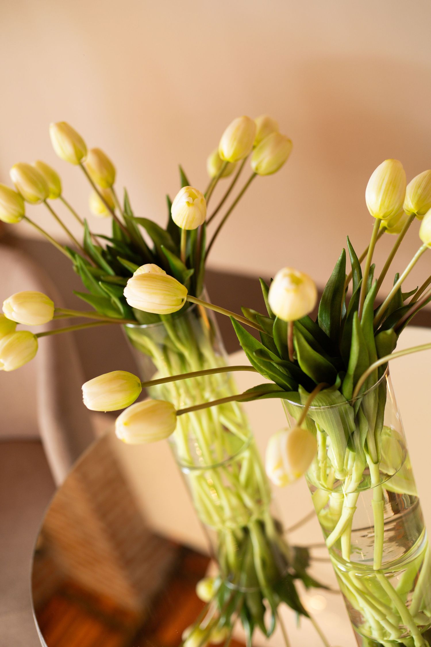 Yellow tulips in clear glass vases on a wooden table, with green stems visible through the water.