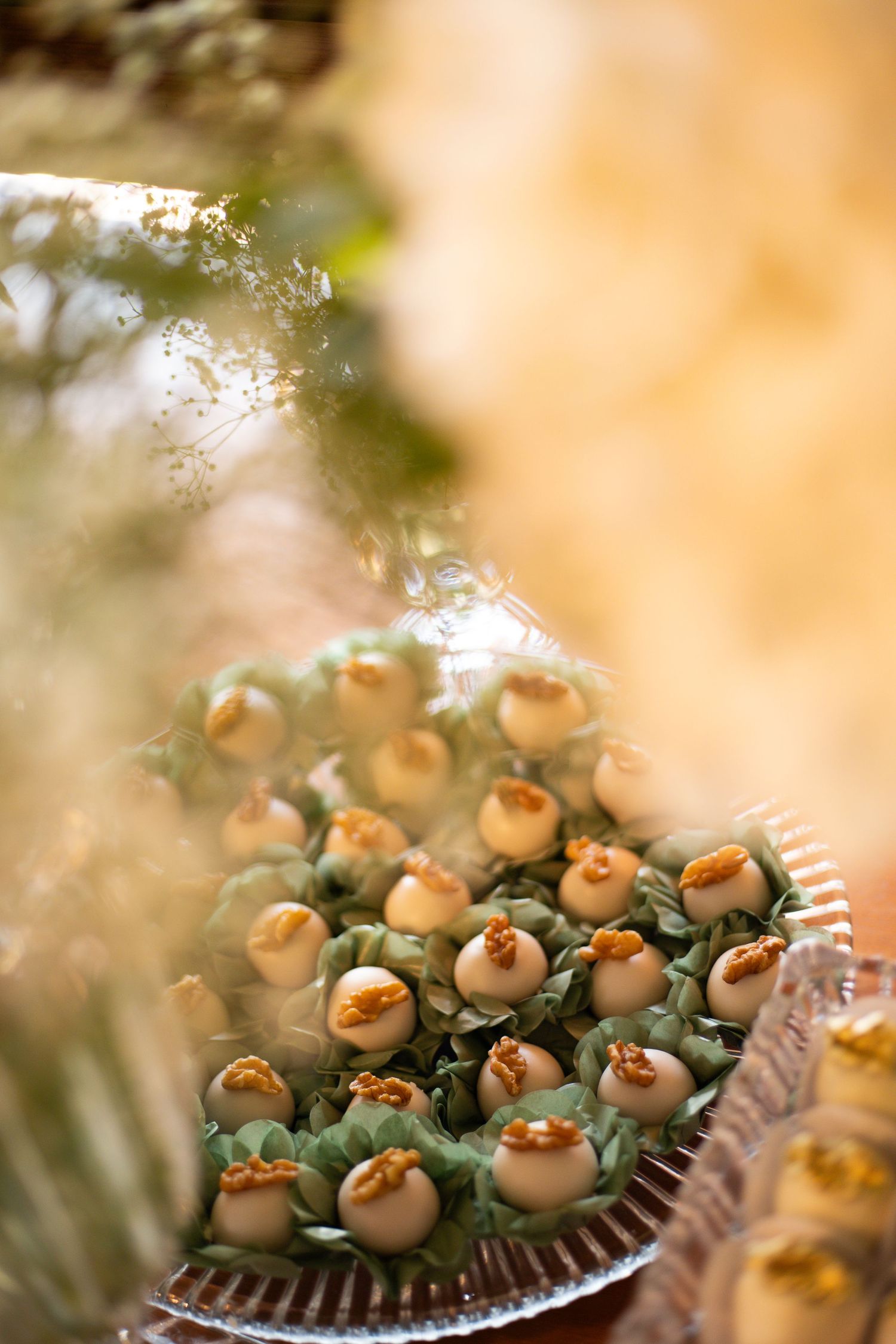 Elegant tray of white chocolate truffles in green cups, topped with golden decorations, displayed at a wedding reception.