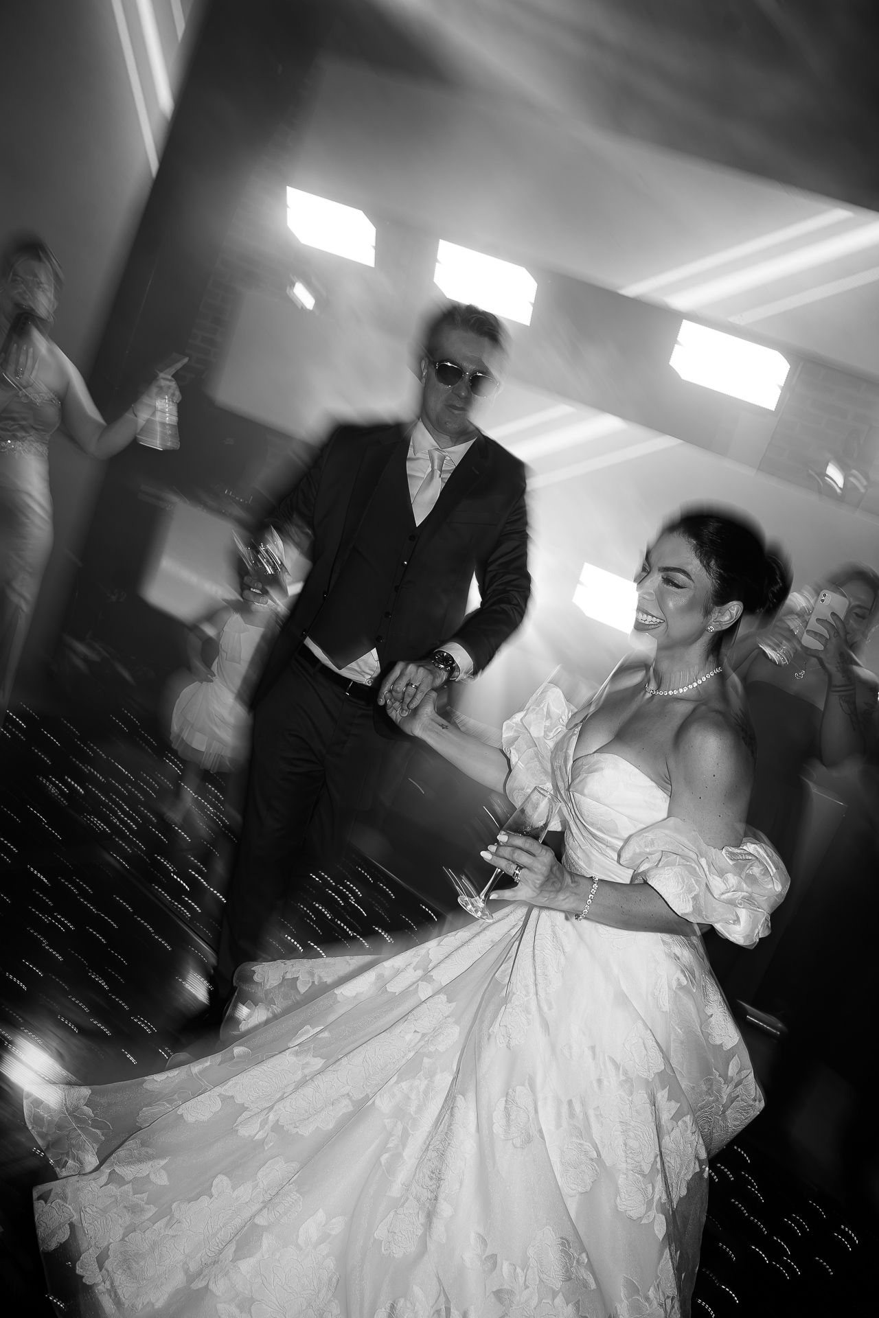 Black and white photo of a bride in a white gown dancing with a groom in a suit at a wedding reception.