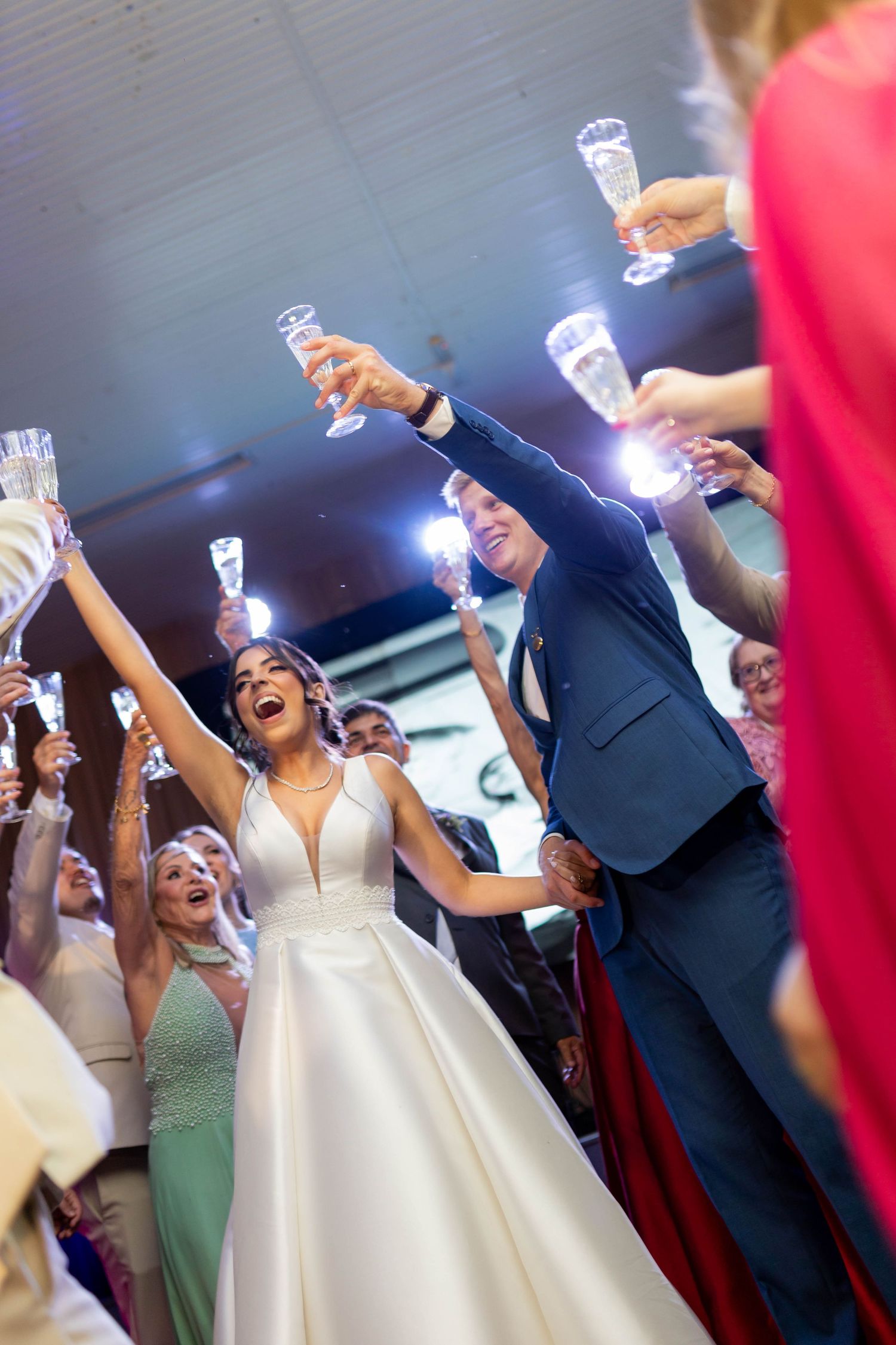 Bride and groom raise champagne glasses with guests during joyful wedding reception toast celebration.