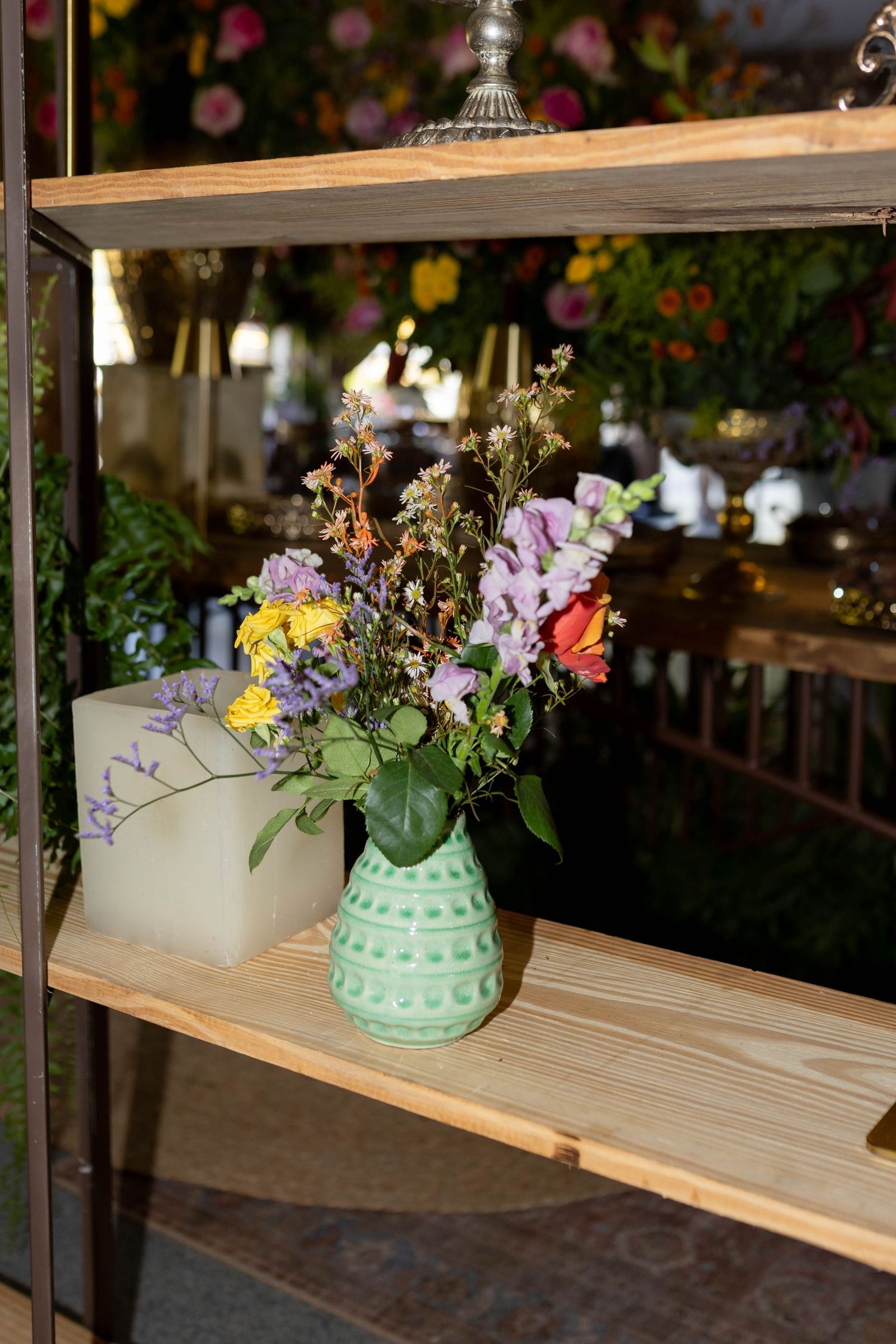 Colorful wildflower bouquet in a green ceramic vase on a wooden shelf in a floral shop.