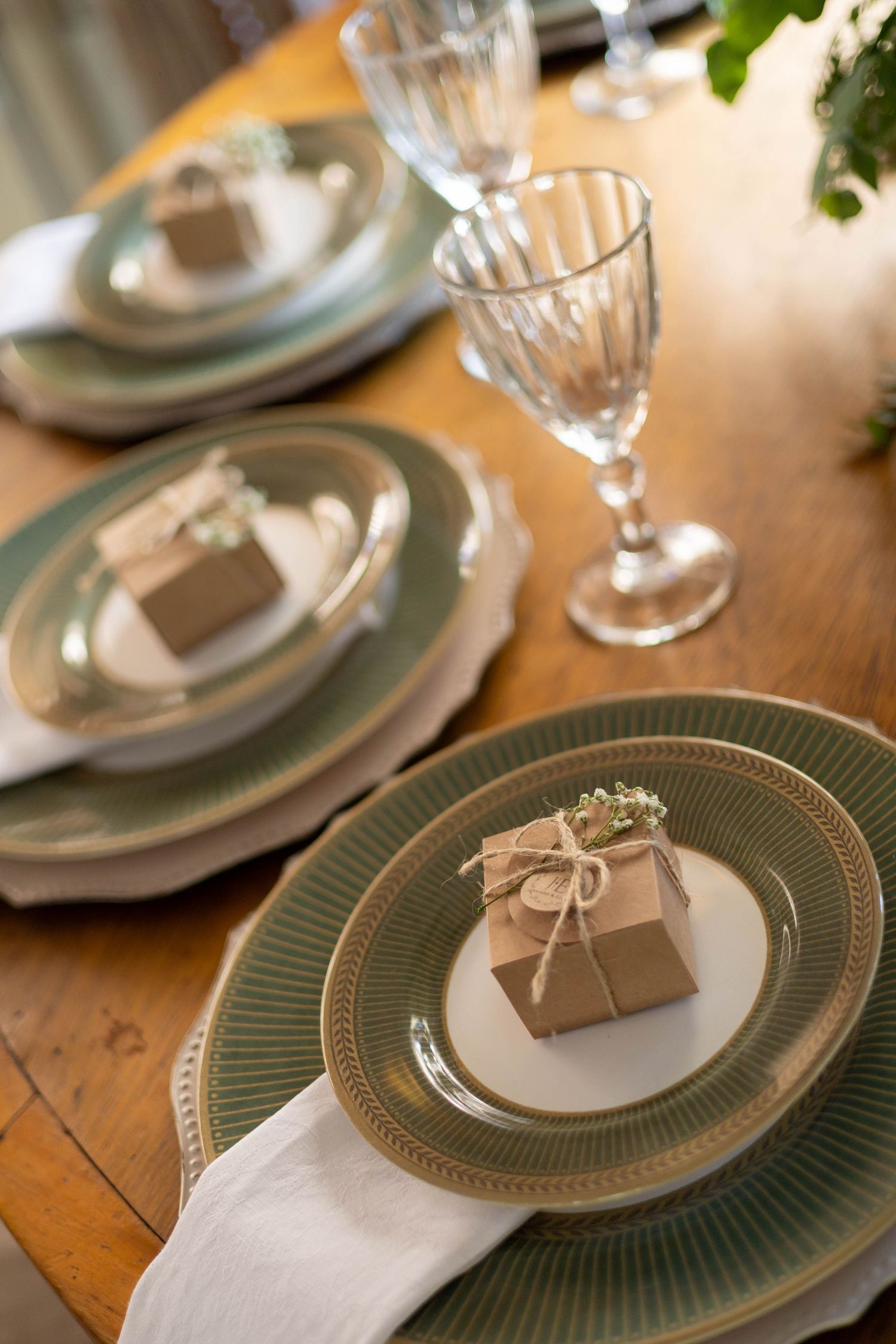 Elegant table setting with green rimmed plates, crystal glasses, and kraft paper gift boxes tied with twine on a wooden table.