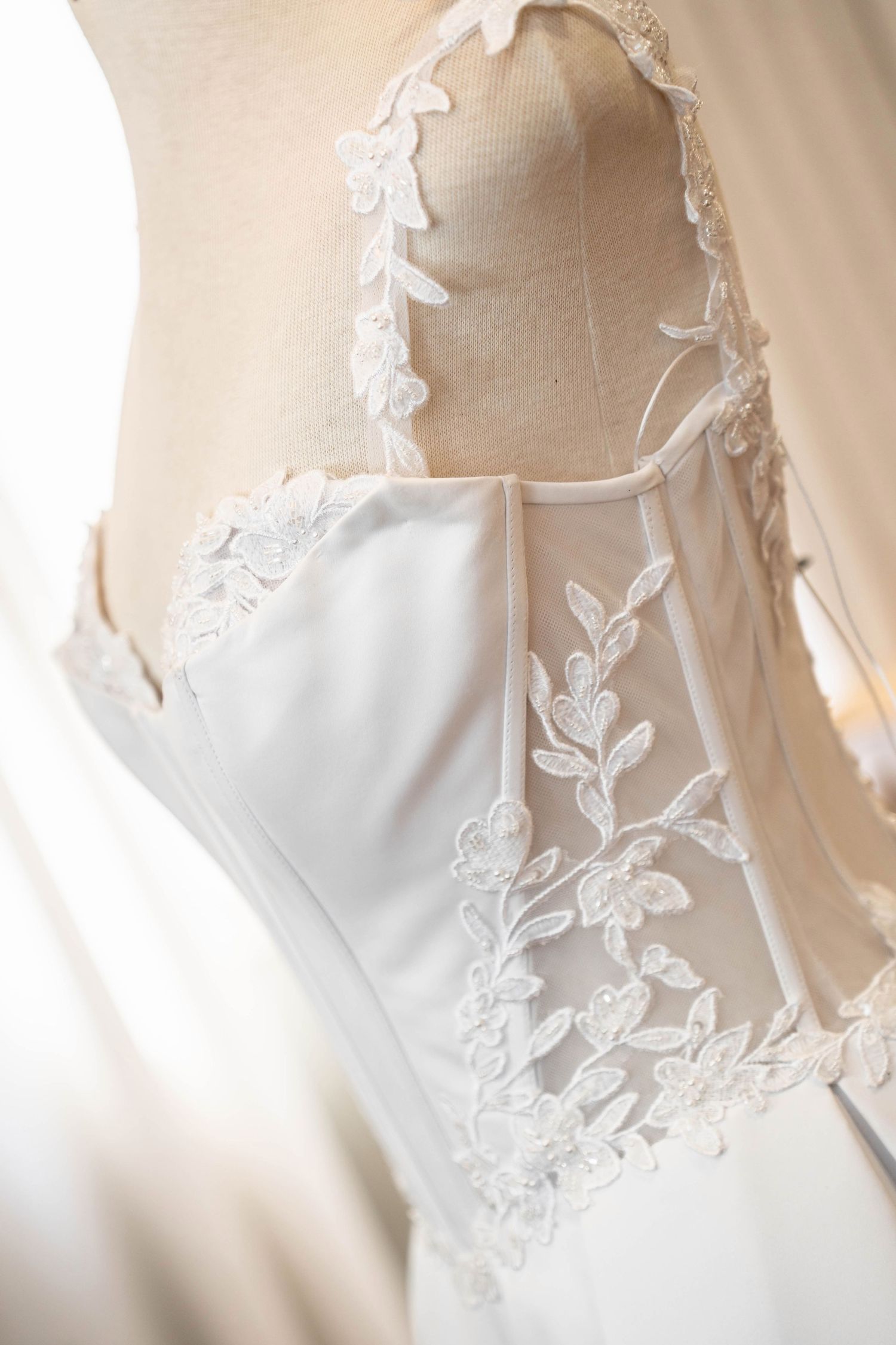 Close-up of an elegant white wedding dress with delicate floral lace detailing on a mannequin.