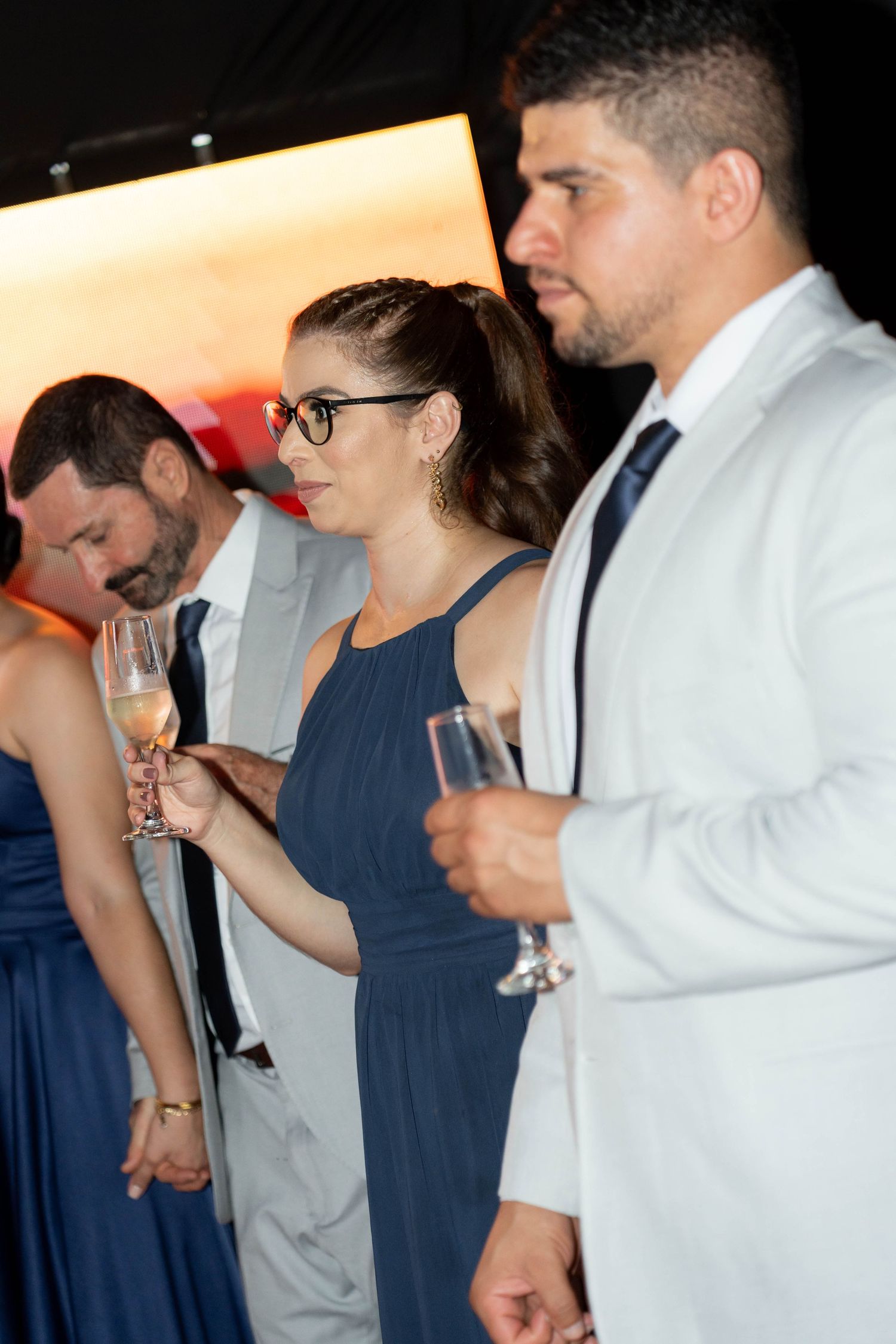 Elegantly dressed guests holding champagne flutes at a formal event, wearing navy and white attire.
