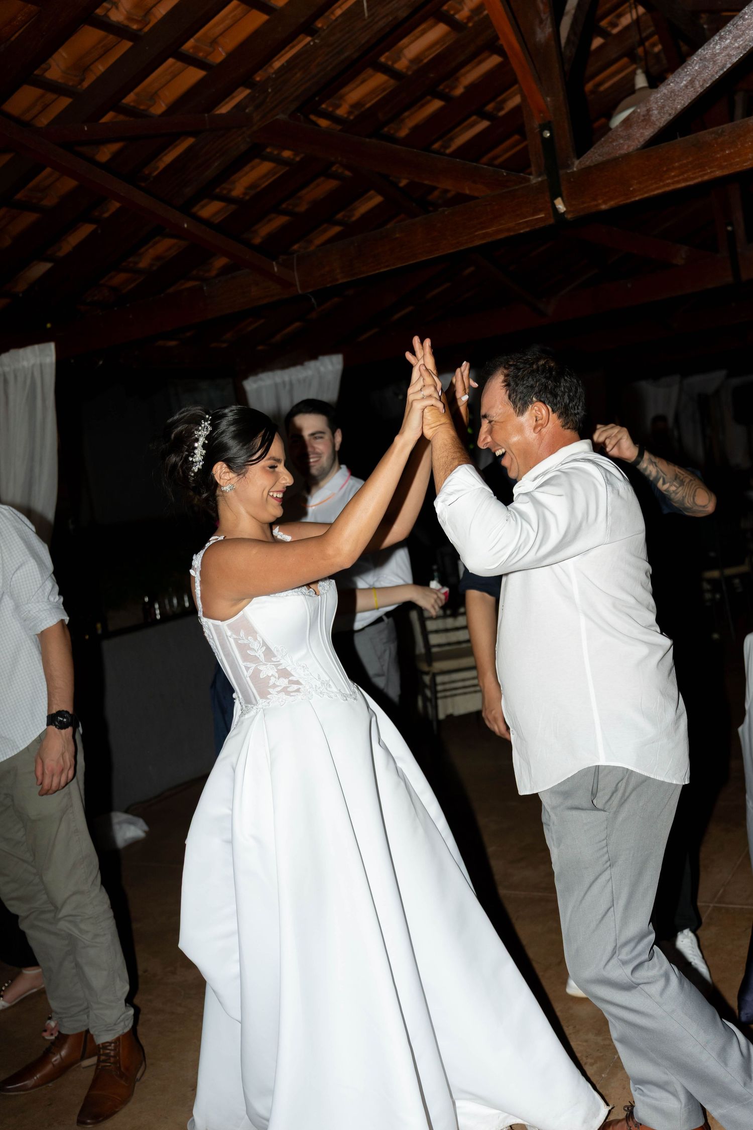Bride and groom dancing joyfully at their wedding reception, holding hands raised in a rustic venue.