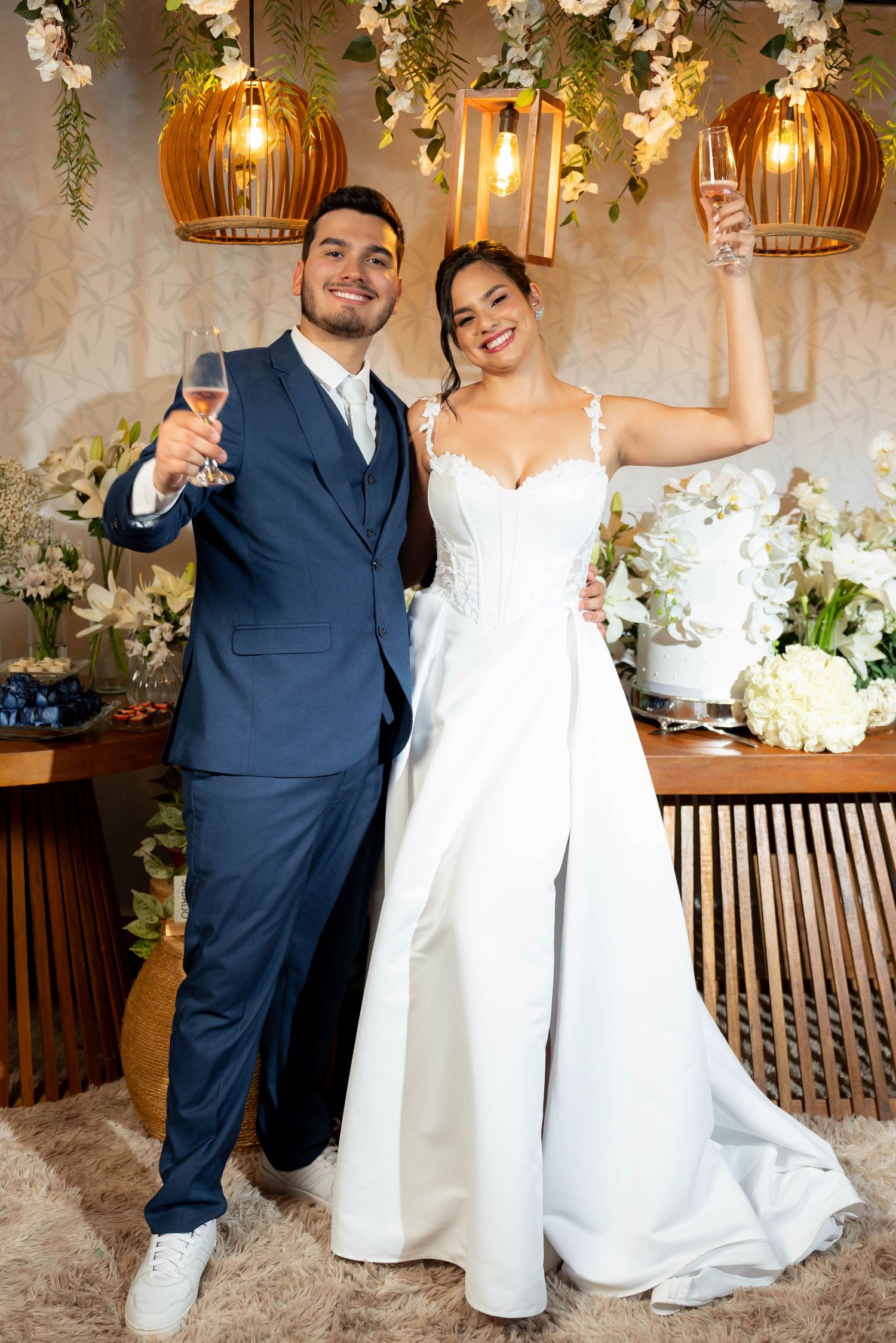 Bride and groom toasting with champagne glasses at their wedding reception, surrounded by floral decorations and warm lighting.