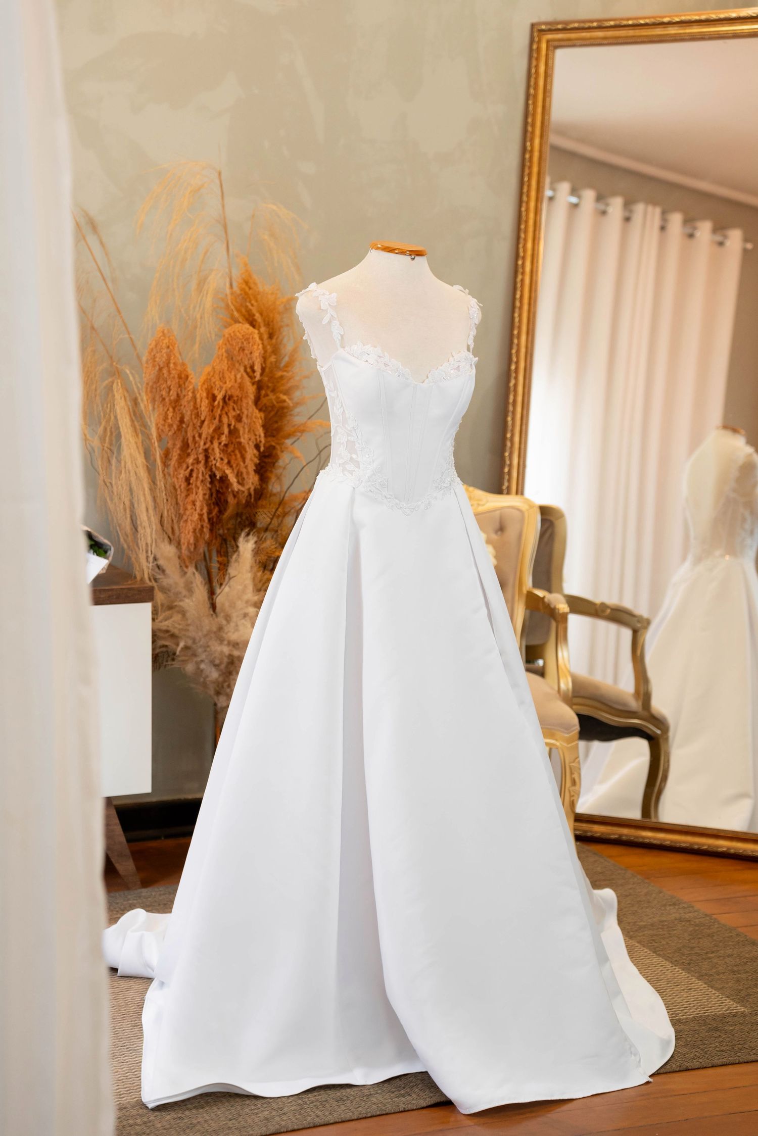 Elegant white A-line wedding gown with lace bodice on mannequin in bridal boutique with gold mirror.