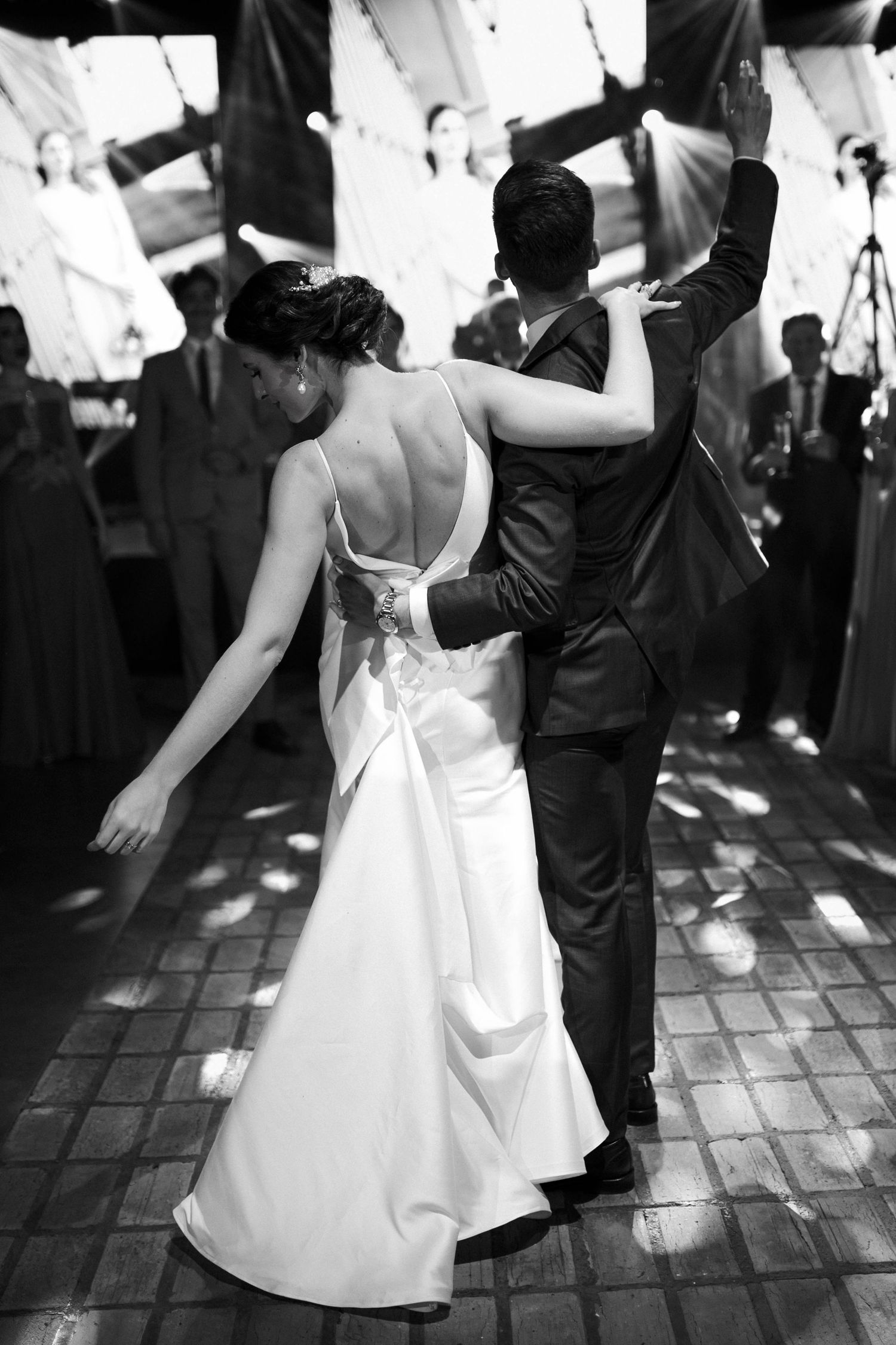 Black and white photo of bride and groom sharing their first dance at a beautifully lit wedding reception.
