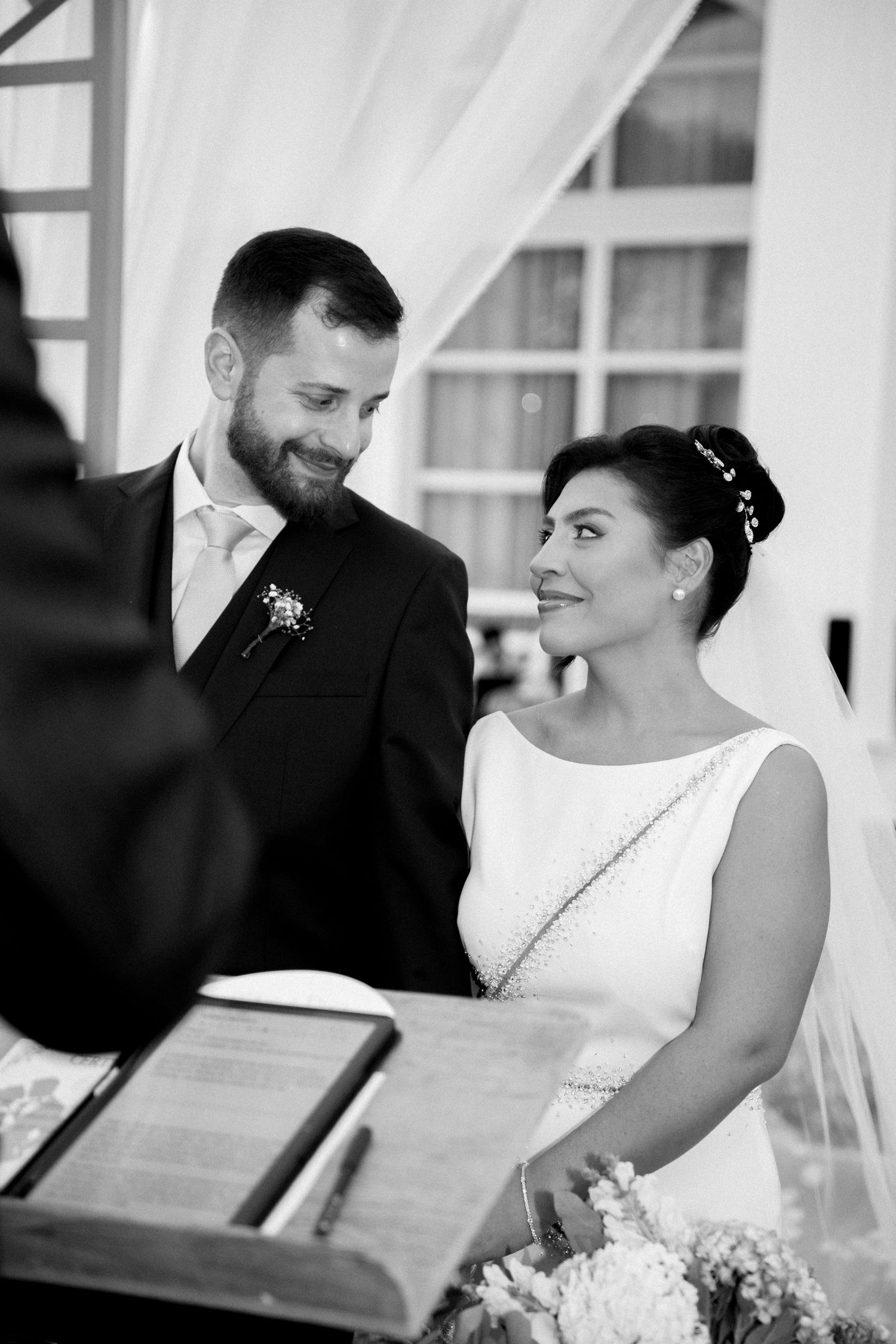 Bride and groom exchange loving glances during their wedding ceremony at a draped outdoor altar.