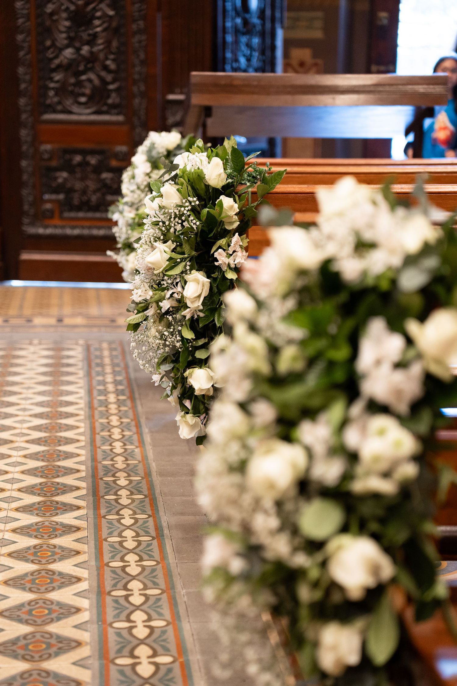 White floral arrangements decorating church pews along a tiled aisle for an elegant wedding ceremony.