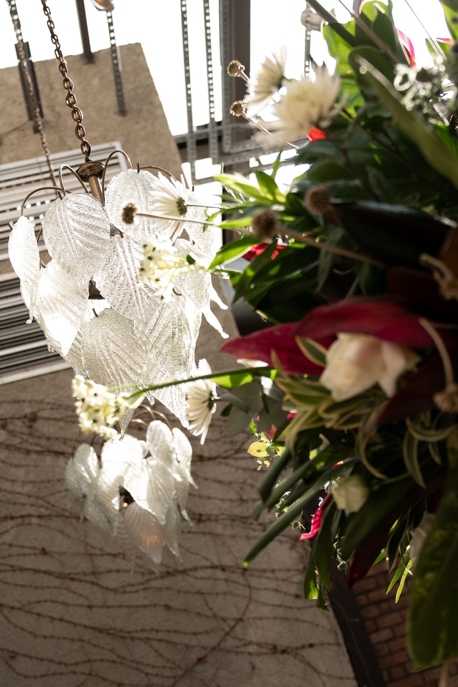 Elegant glass petal chandelier hanging near a vibrant floral arrangement with pink and white blooms indoors.