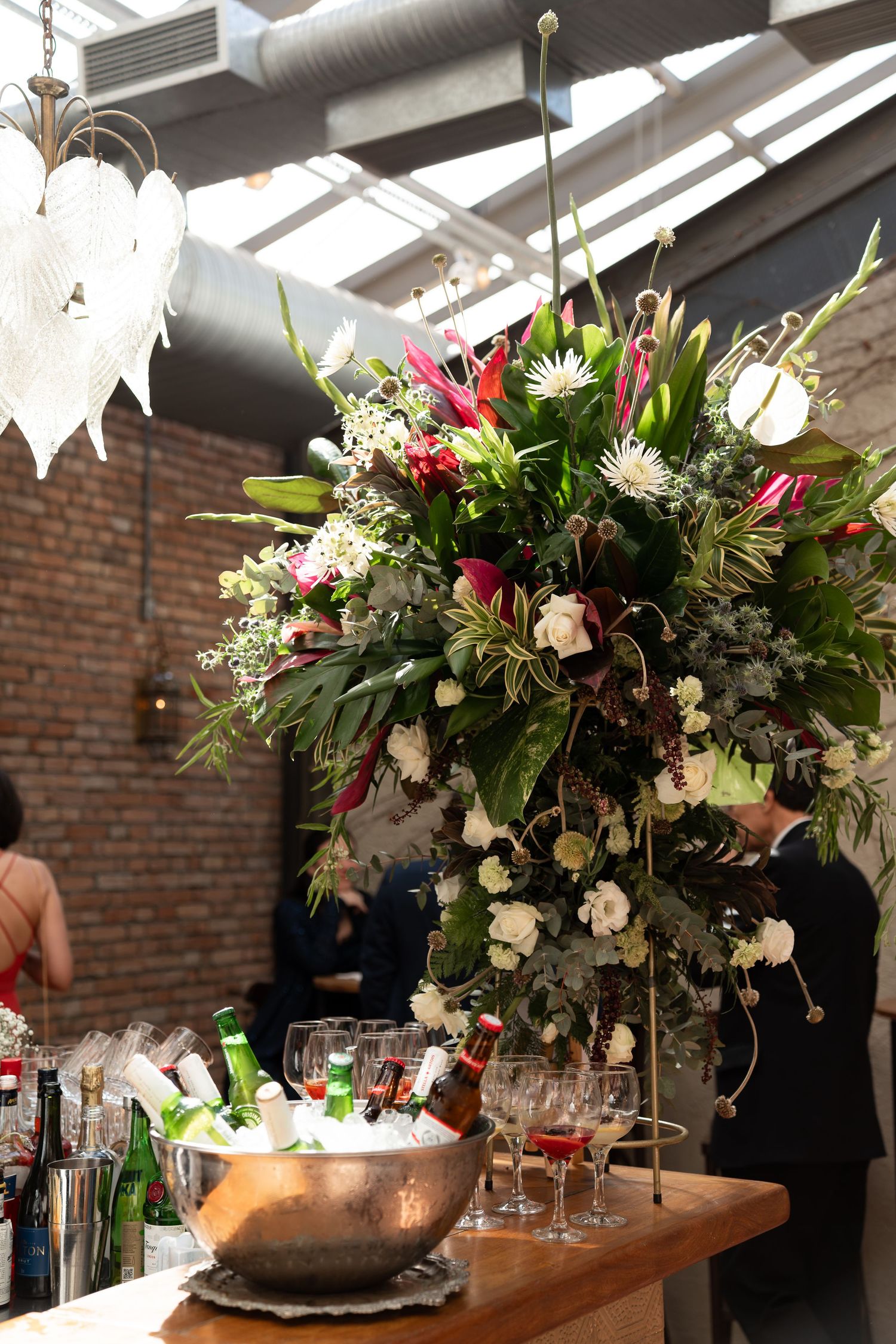 Elegant event bar setup with lush floral arrangement, wine glasses, and chilled bottles on a wooden table.