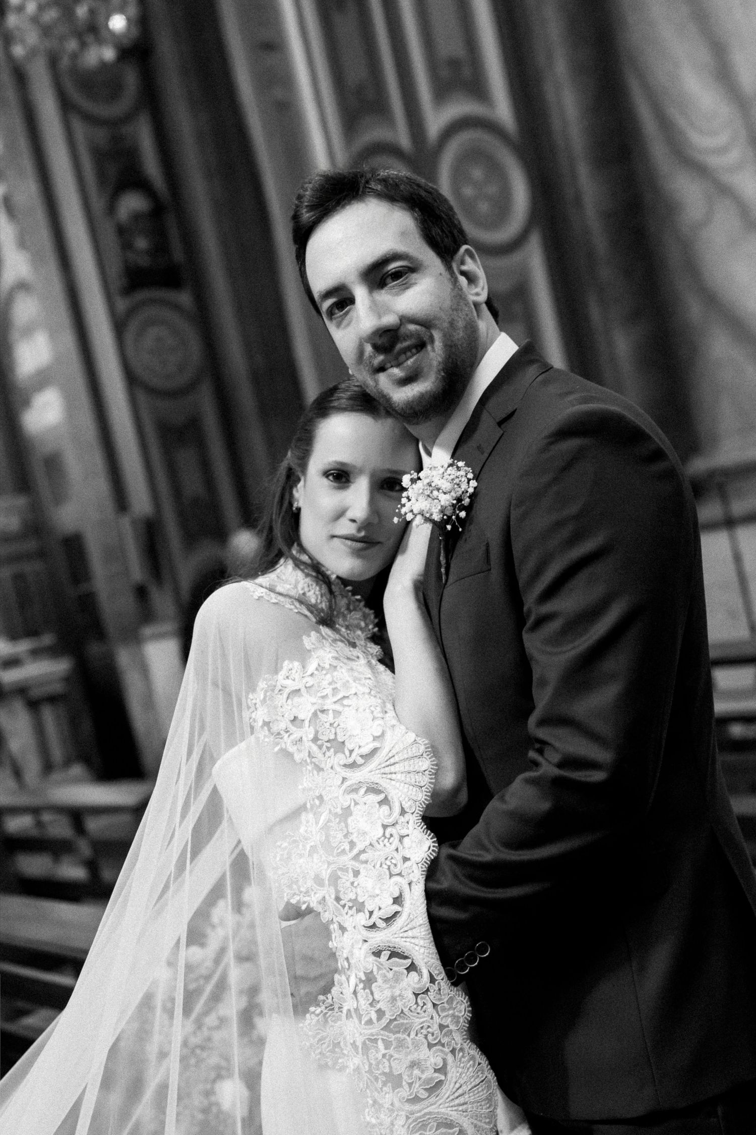 Black and white wedding photo of a smiling bride and groom posing elegantly inside a grand church.