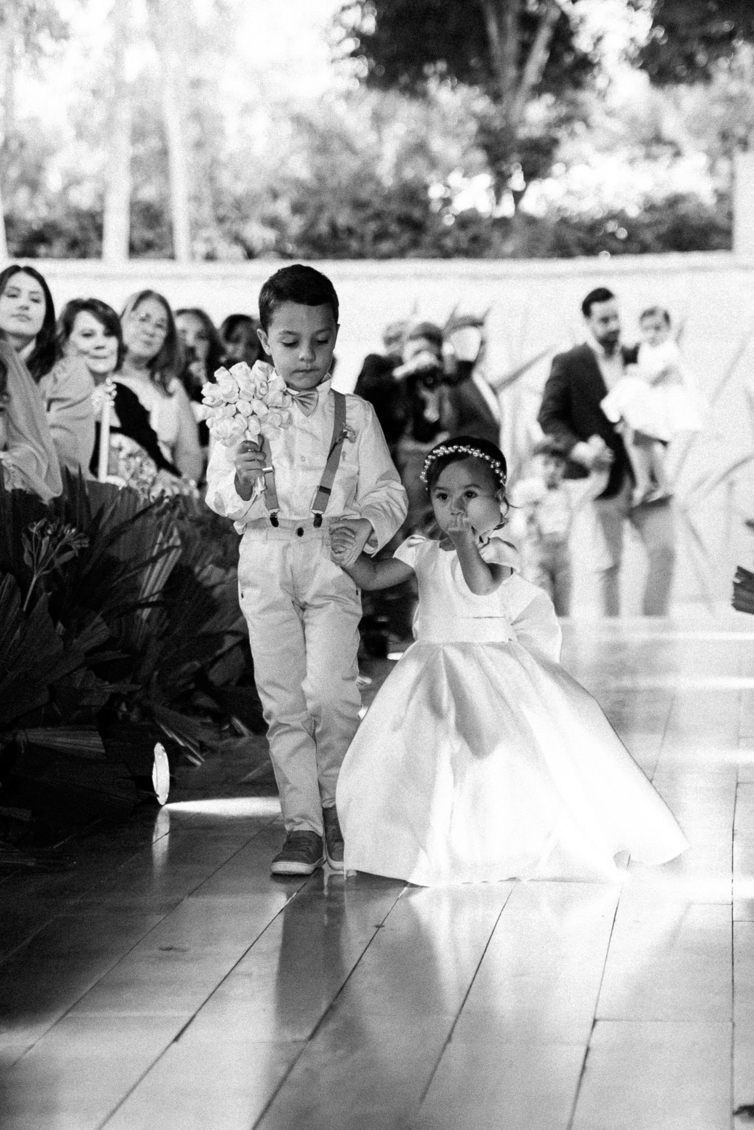 Black and white photo of a ring bearer and flower girl walking down the aisle at a wedding ceremony.