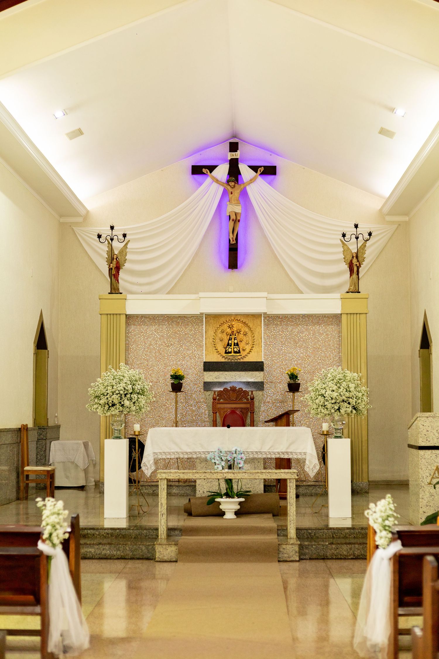 Elegant Catholic church interior with crucifix, white floral arrangements, and altar decorated for a wedding ceremony.