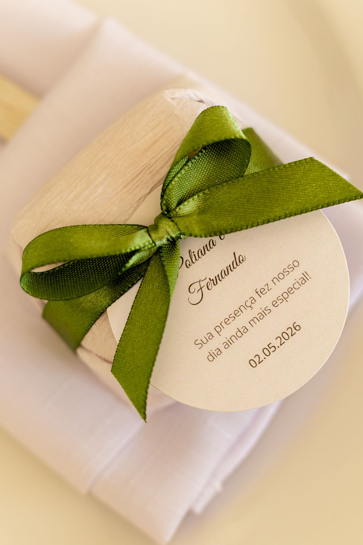 Wedding favor gift box with green ribbon bow and round tag reading Poliana and Fernando, 02.05.2026.