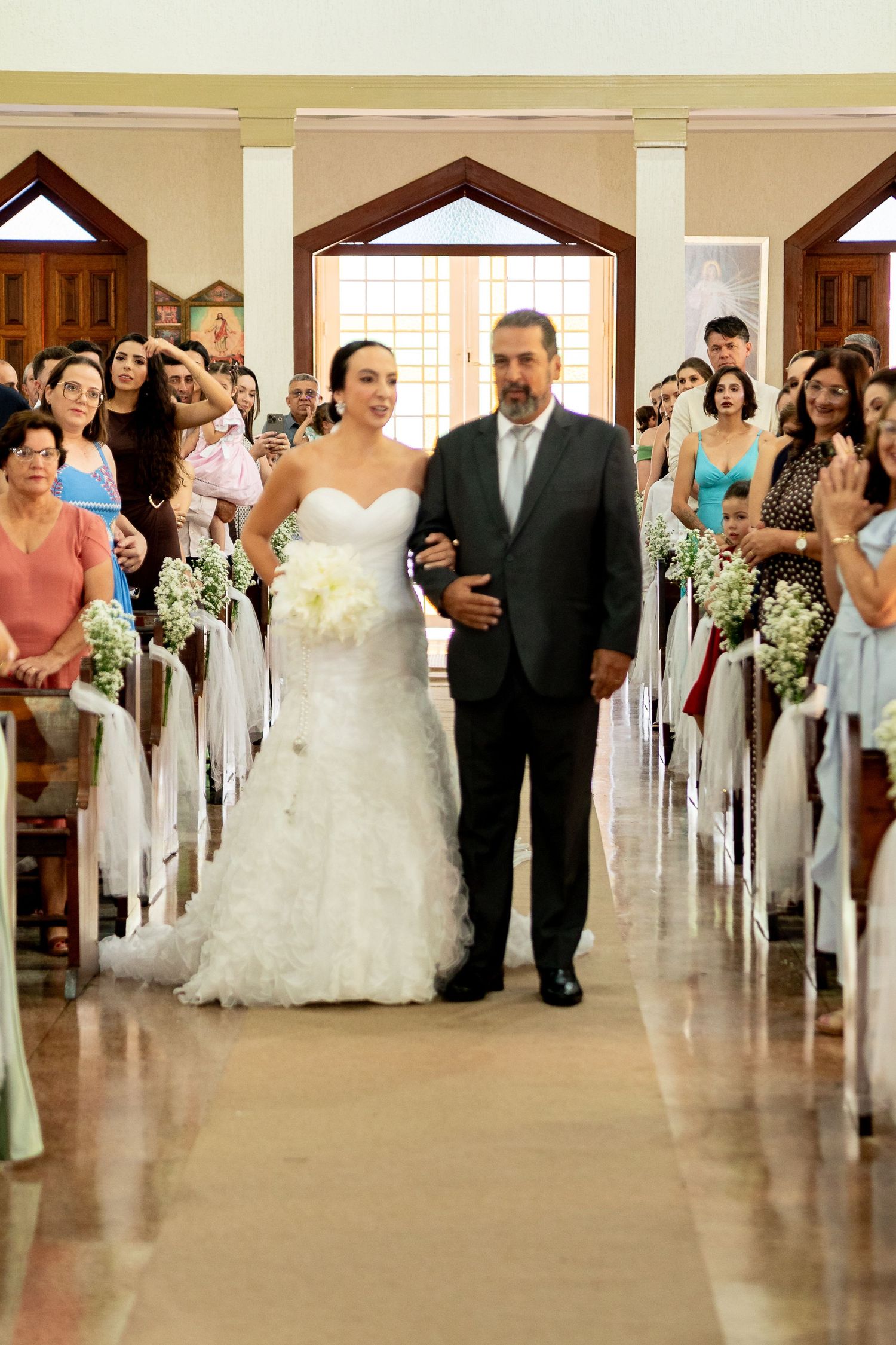 Bride in white gown walks down church aisle with father during wedding ceremony, guests seated in pews.