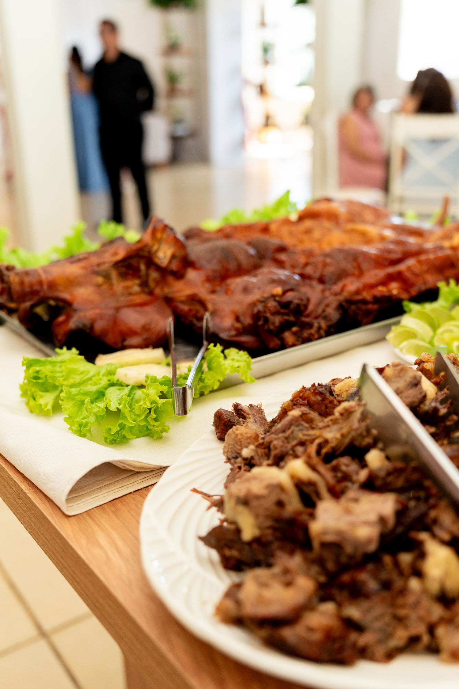 Roasted whole pig on a buffet table with carved meat on a plate, garnished with fresh lettuce leaves.