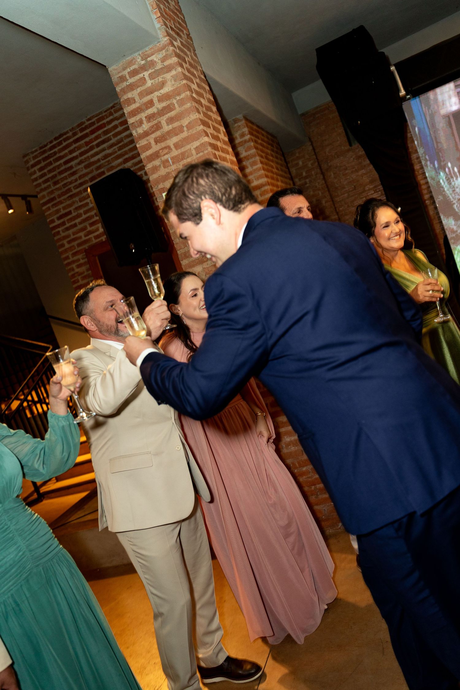 Guests in formal attire toast with champagne glasses at an elegant indoor wedding reception venue.