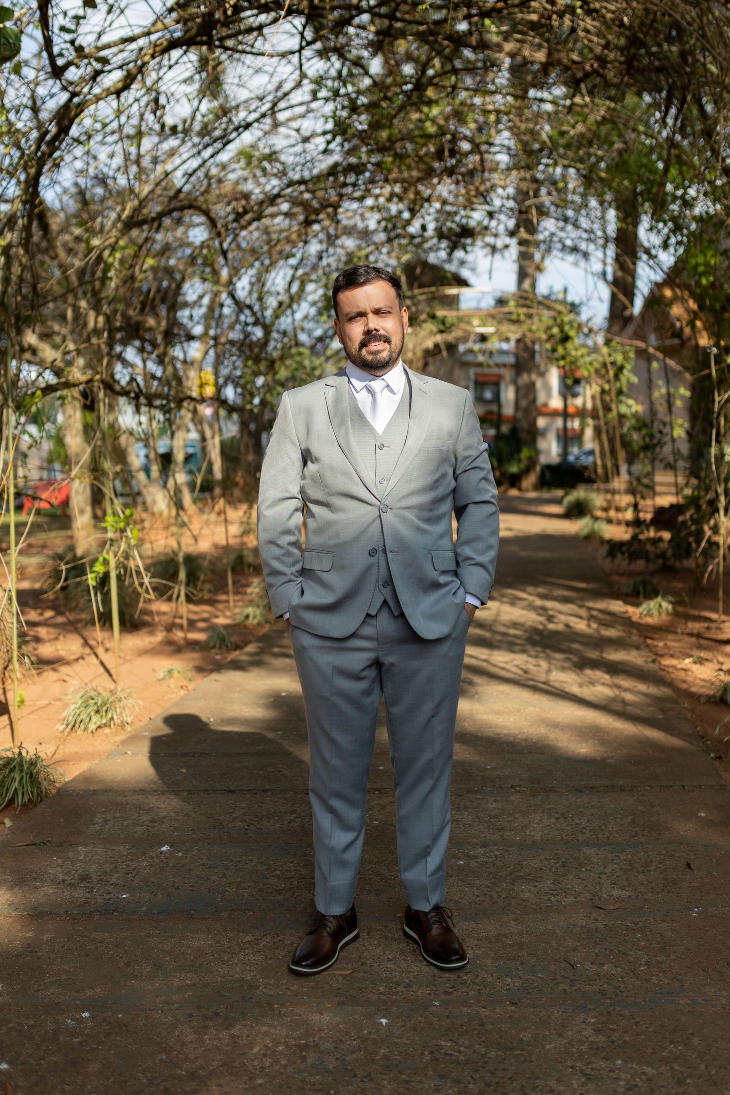 Man in gray three-piece suit standing on garden path surrounded by trees.