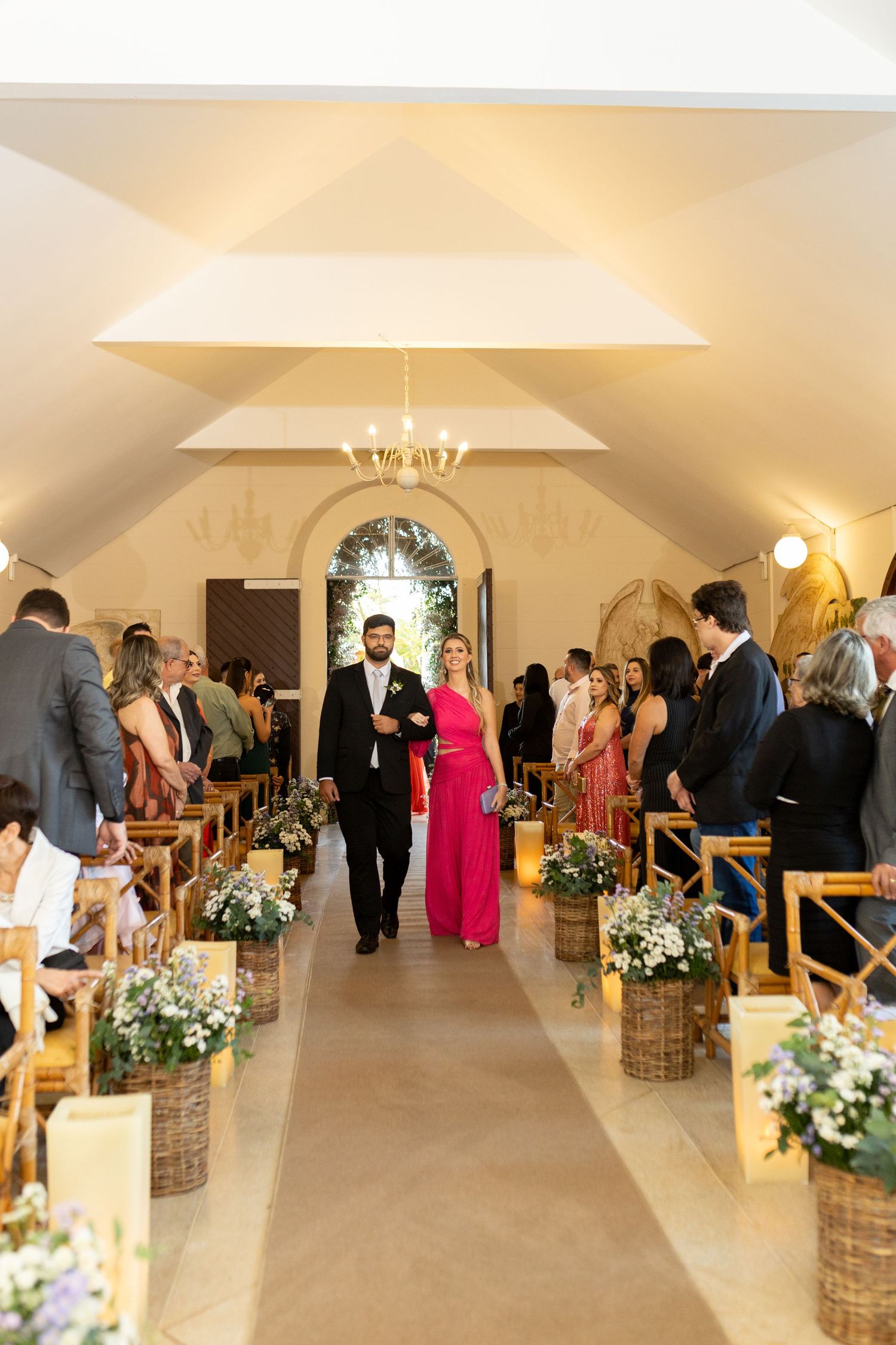 Elegant wedding ceremony in a chapel with guests seated as a couple walks down the flower-decorated aisle.