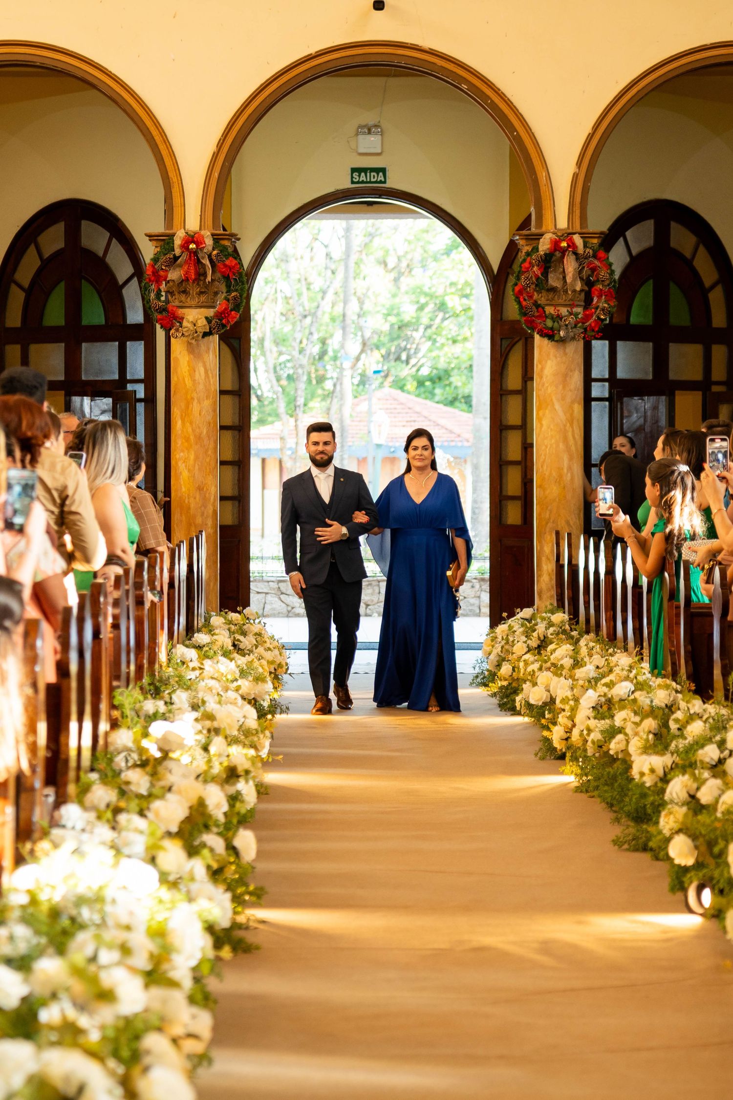 Couple walks down flower-lined church aisle during wedding ceremony, woman in blue gown, man in dark suit.