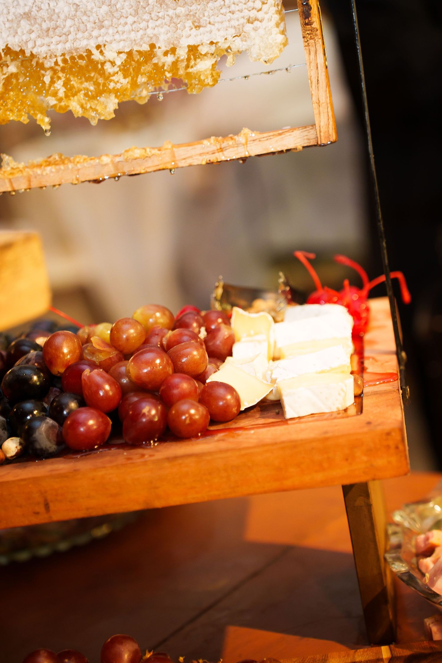 Wooden display board with red and black grapes, white cheese, and honeycomb frame at a gourmet food market.