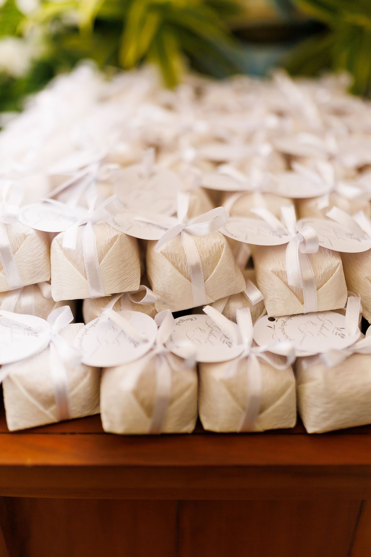 Elegant white wedding favor boxes tied with satin ribbons displayed on a wooden table at a reception.