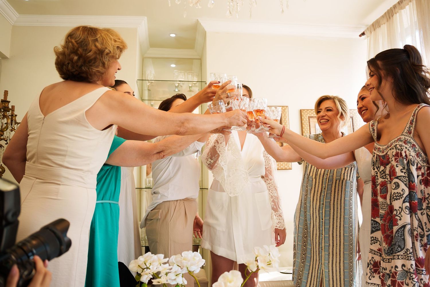 Women in elegant dresses toasting with champagne glasses at a bridal party celebration indoors.