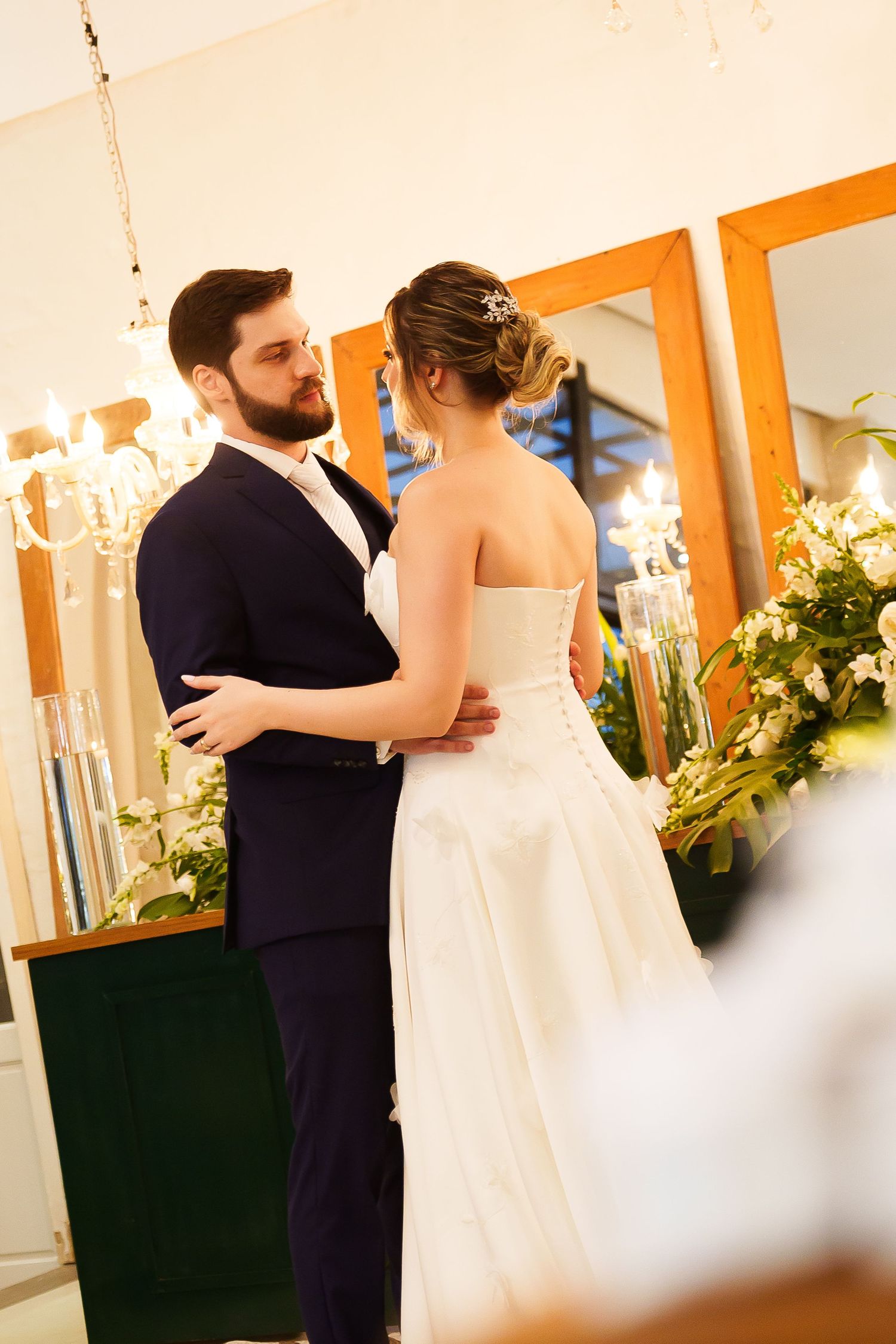 Bride and groom share a romantic moment at their wedding reception, surrounded by candles and white floral arrangements.