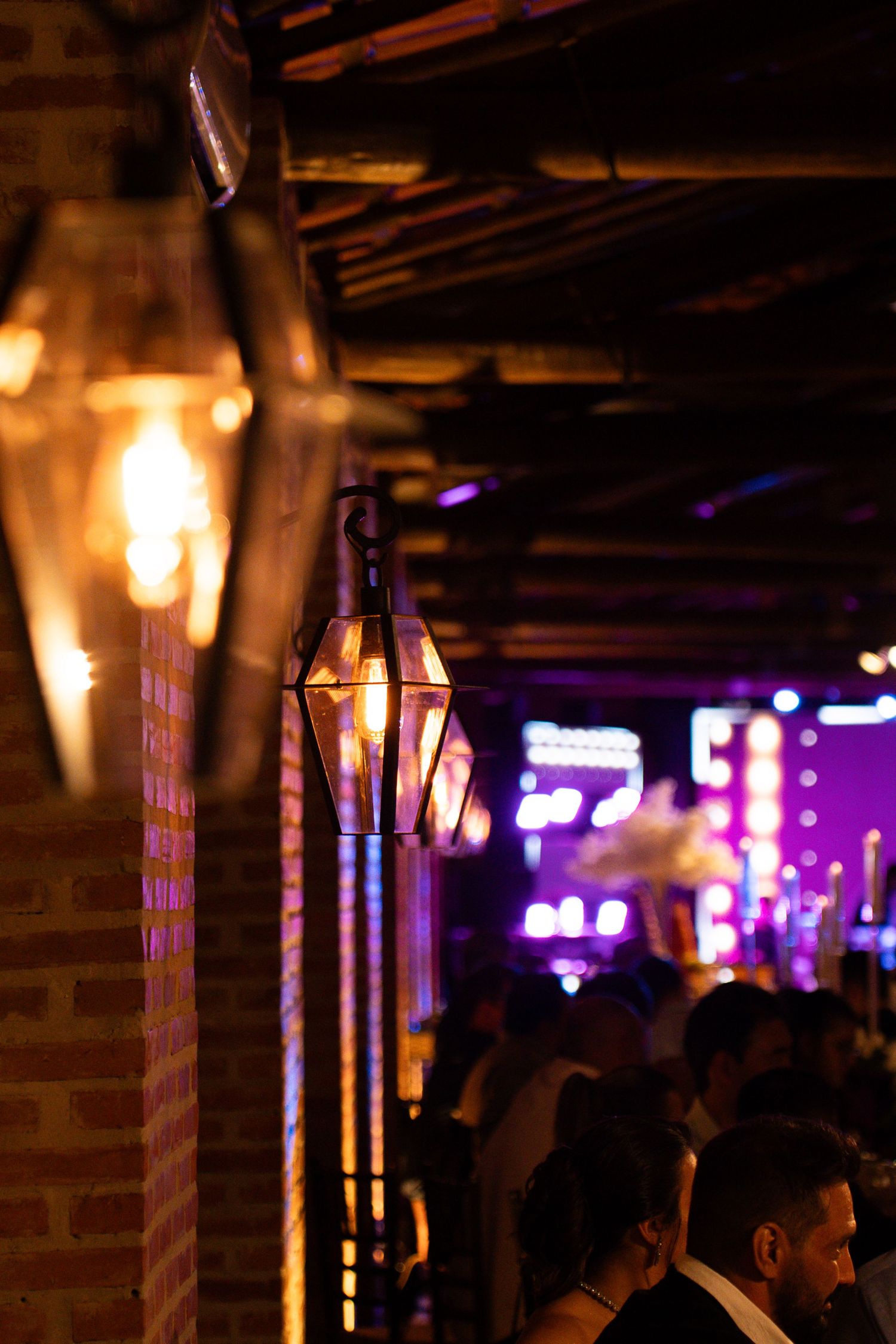 Vintage gas lanterns mounted on brick wall illuminate a lively nightclub with purple neon lights and crowd.