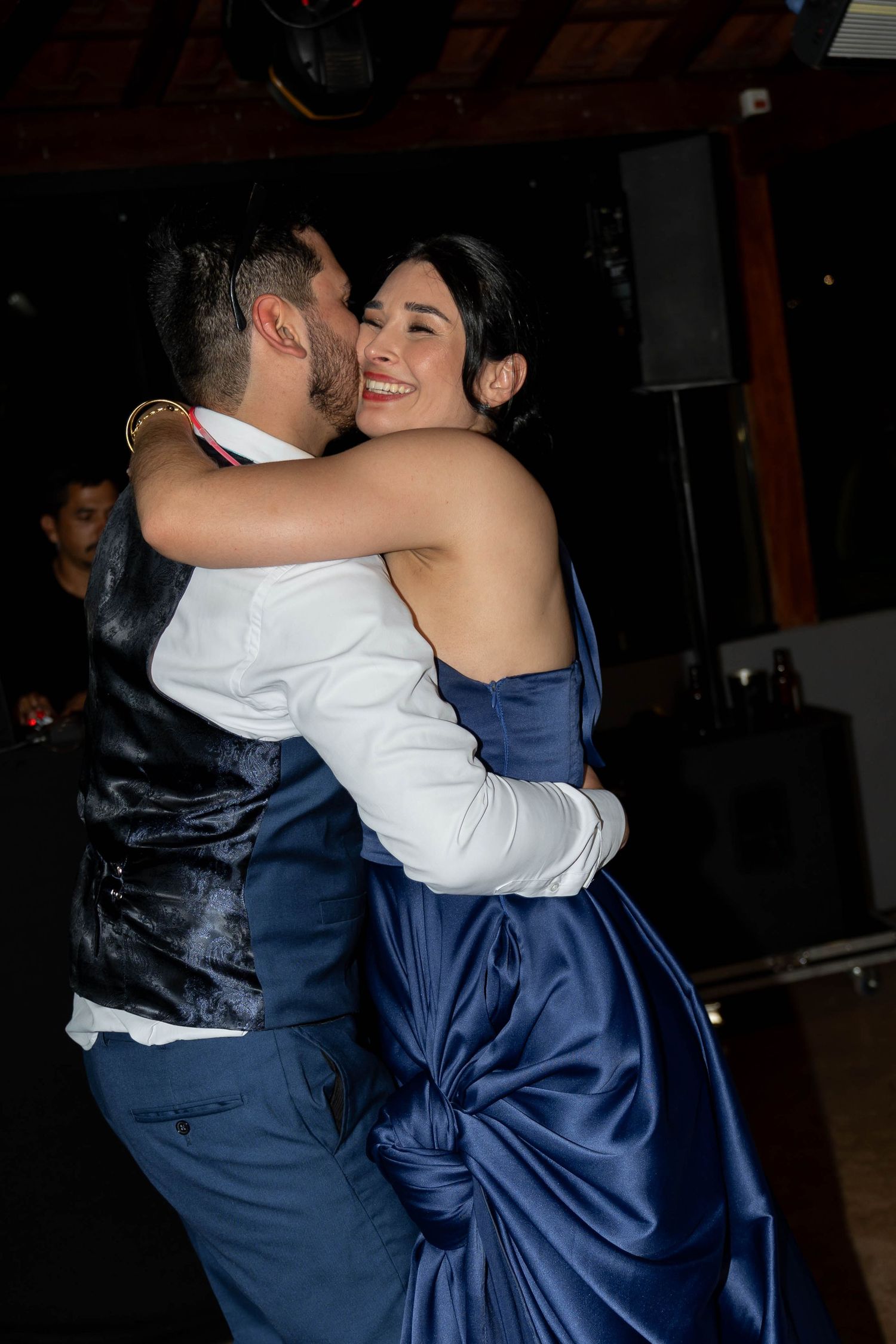 Couple sharing a romantic dance, woman in blue satin gown smiling joyfully at formal evening event.