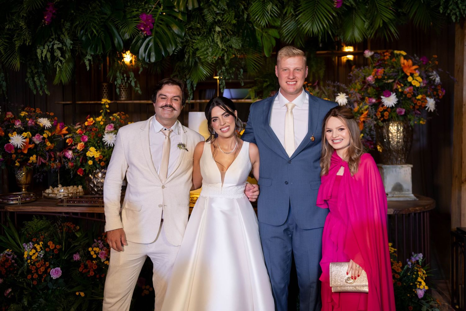 Two couples posing together at a wedding reception surrounded by tropical floral arrangements.