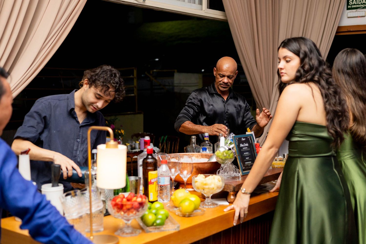 Guests socializing around a well-stocked outdoor bar with a bartender mixing cocktails at a night event.