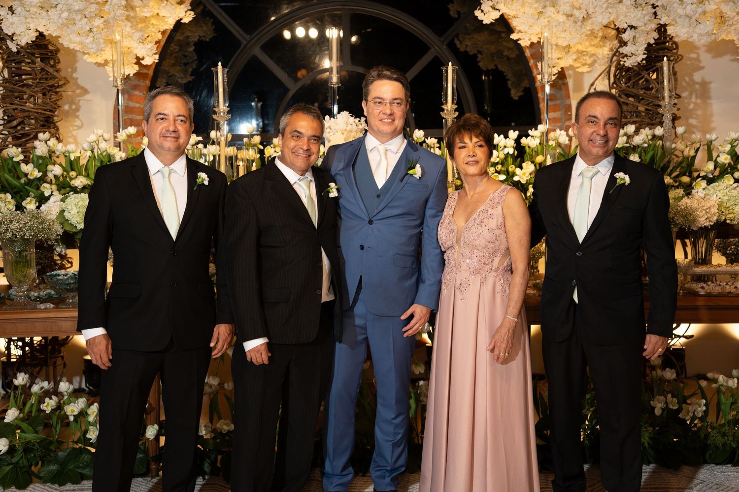 Five elegantly dressed guests pose together at a floral-decorated wedding reception venue.