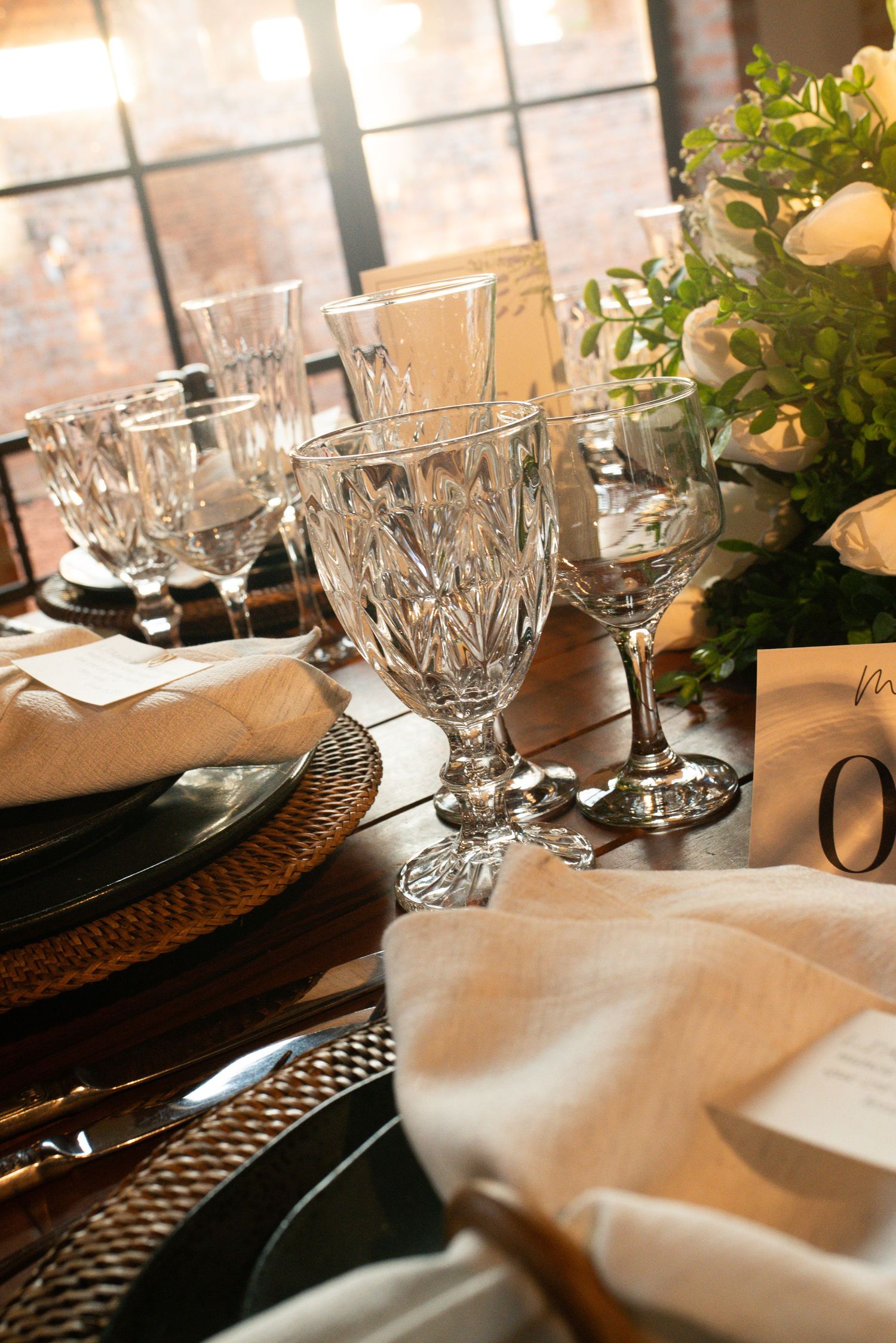 Elegant crystal wine glasses and white linen napkins on a formal dining table with floral centerpiece.