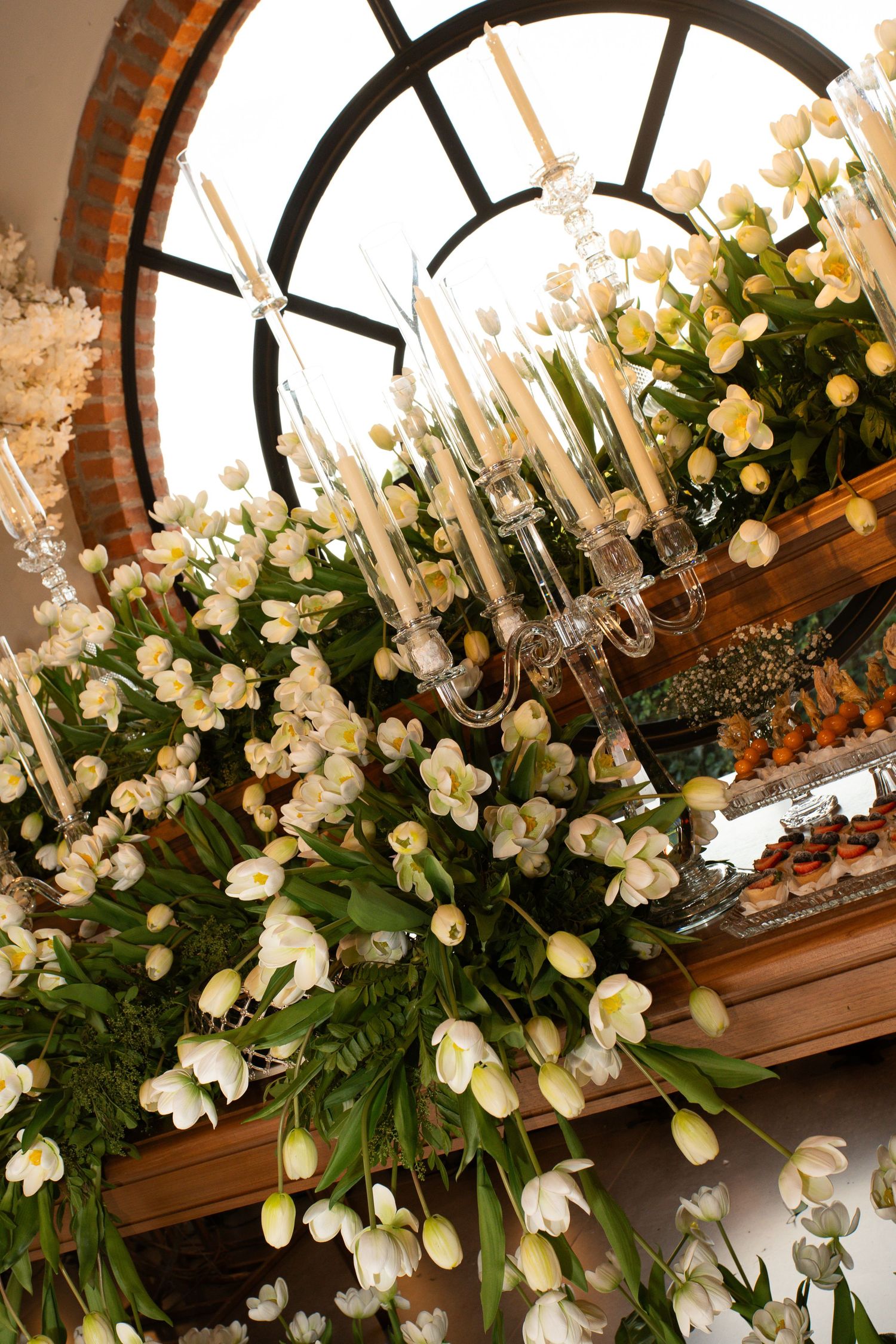 Elegant wedding decor with white tulips, candelabra, and floral arrangements framed by an arched window.