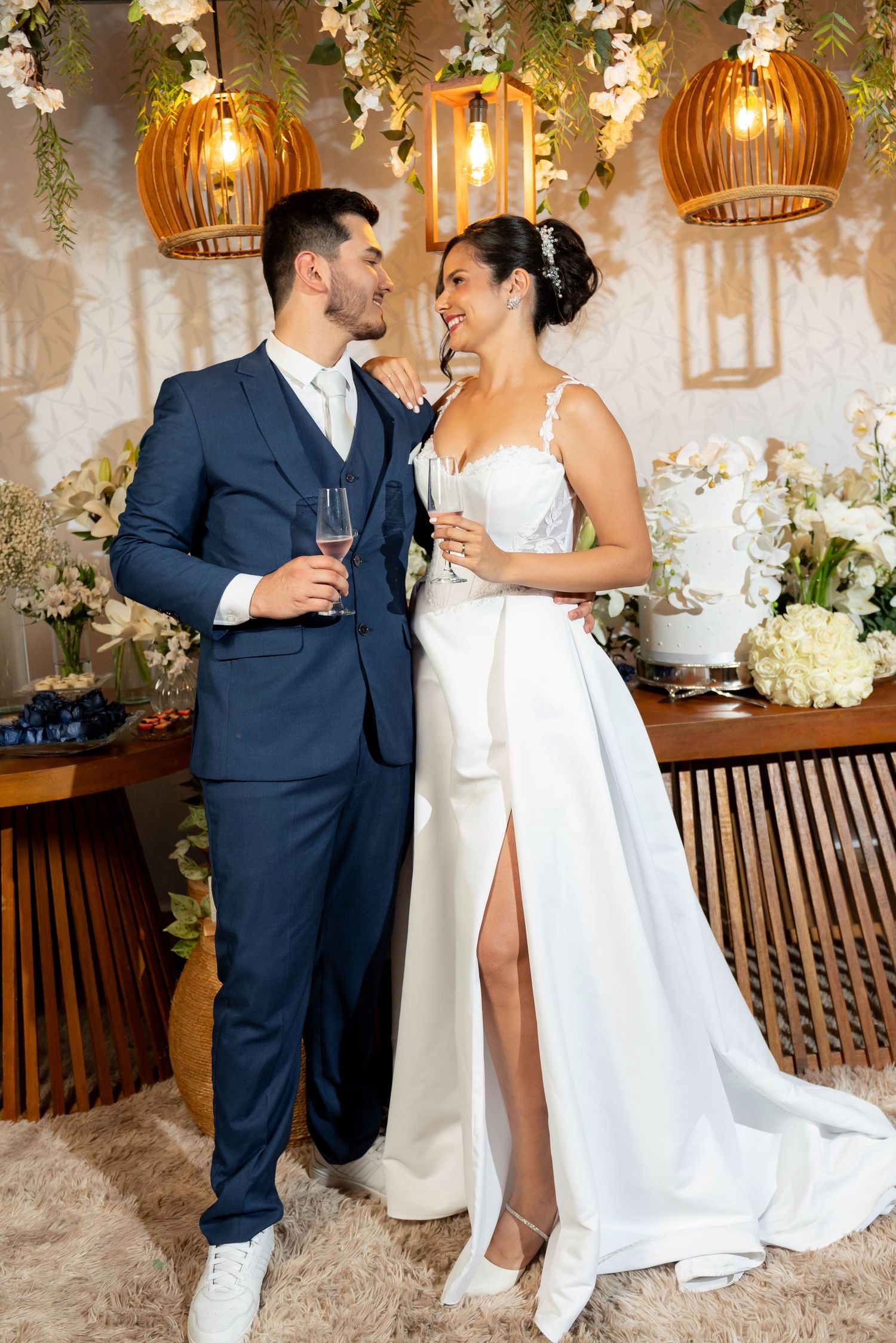 Bride and groom in elegant wedding attire toasting with champagne glasses at a beautifully decorated reception venue.