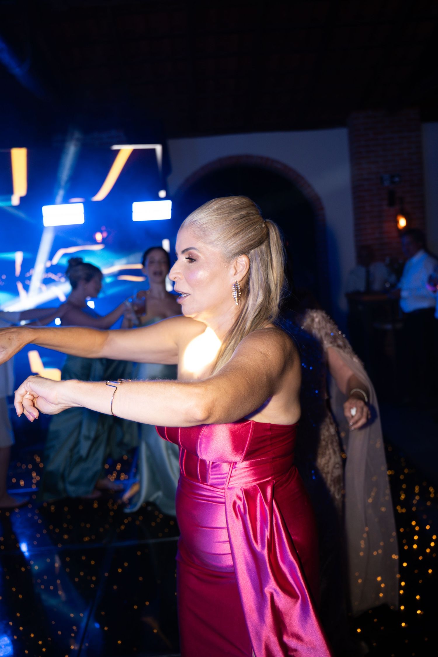 Blonde woman in red satin gown dancing at an elegant evening event with blue stage lighting.