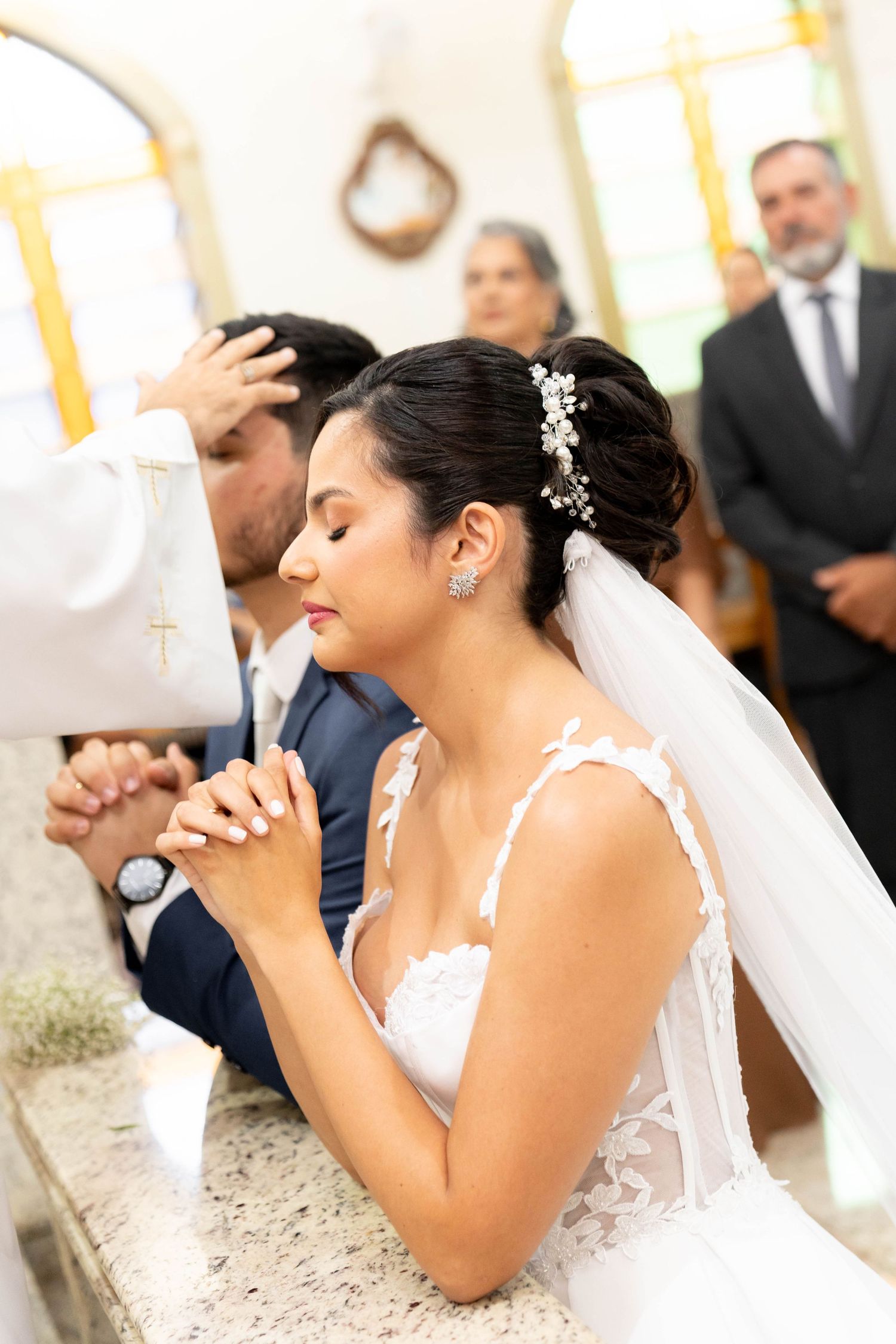 Bride and groom kneeling in prayer during a church wedding ceremony, bride wearing white lace dress and veil.