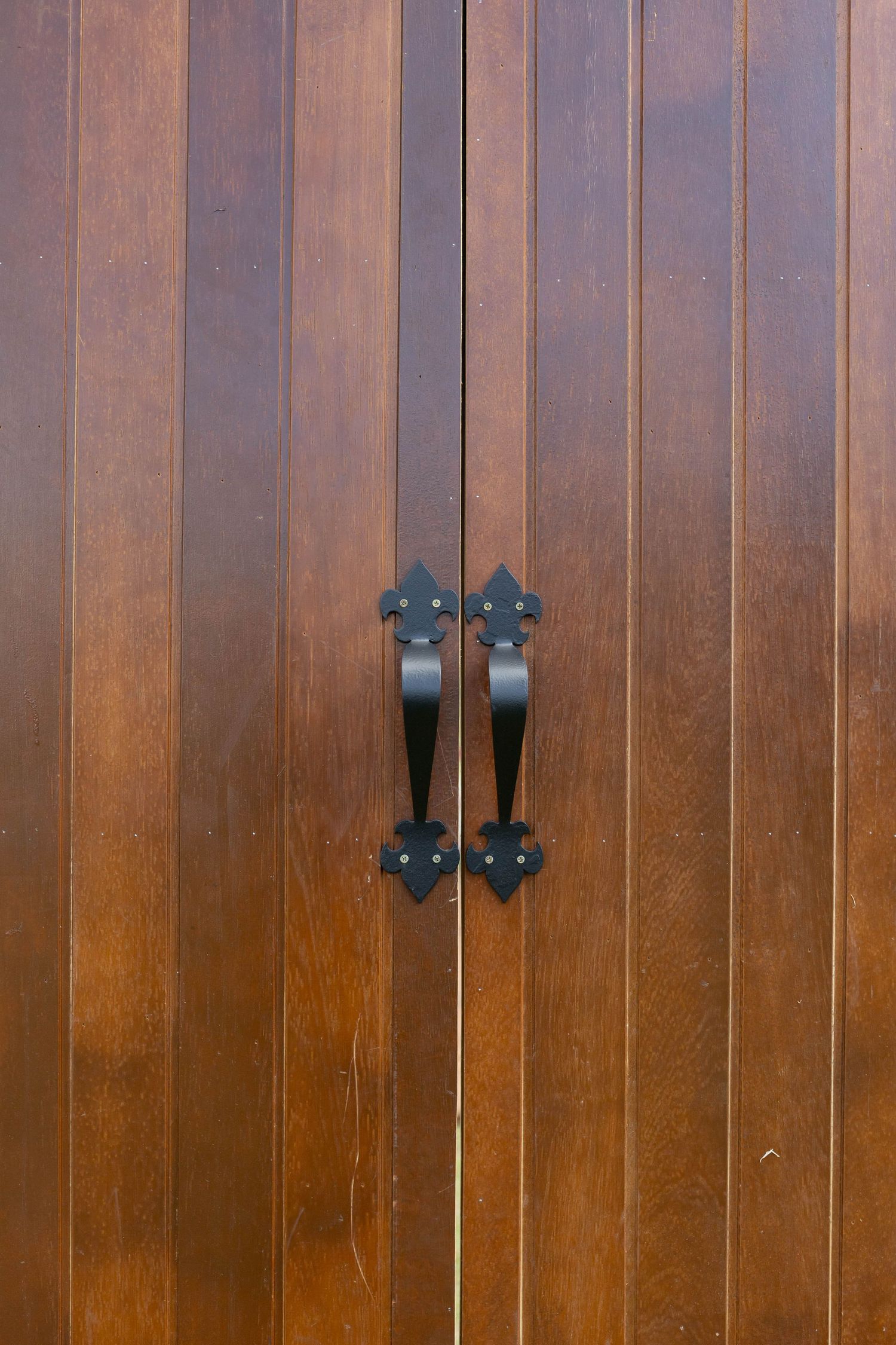 Elegant wooden double doors with ornate black metal handles in a classic fleur-de-lis design.