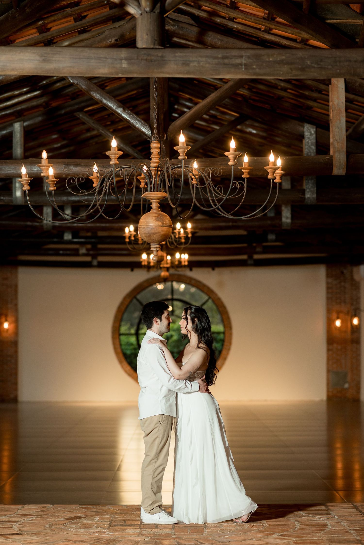 Bride and groom share first dance under rustic chandelier in elegant barn venue with warm candlelight.